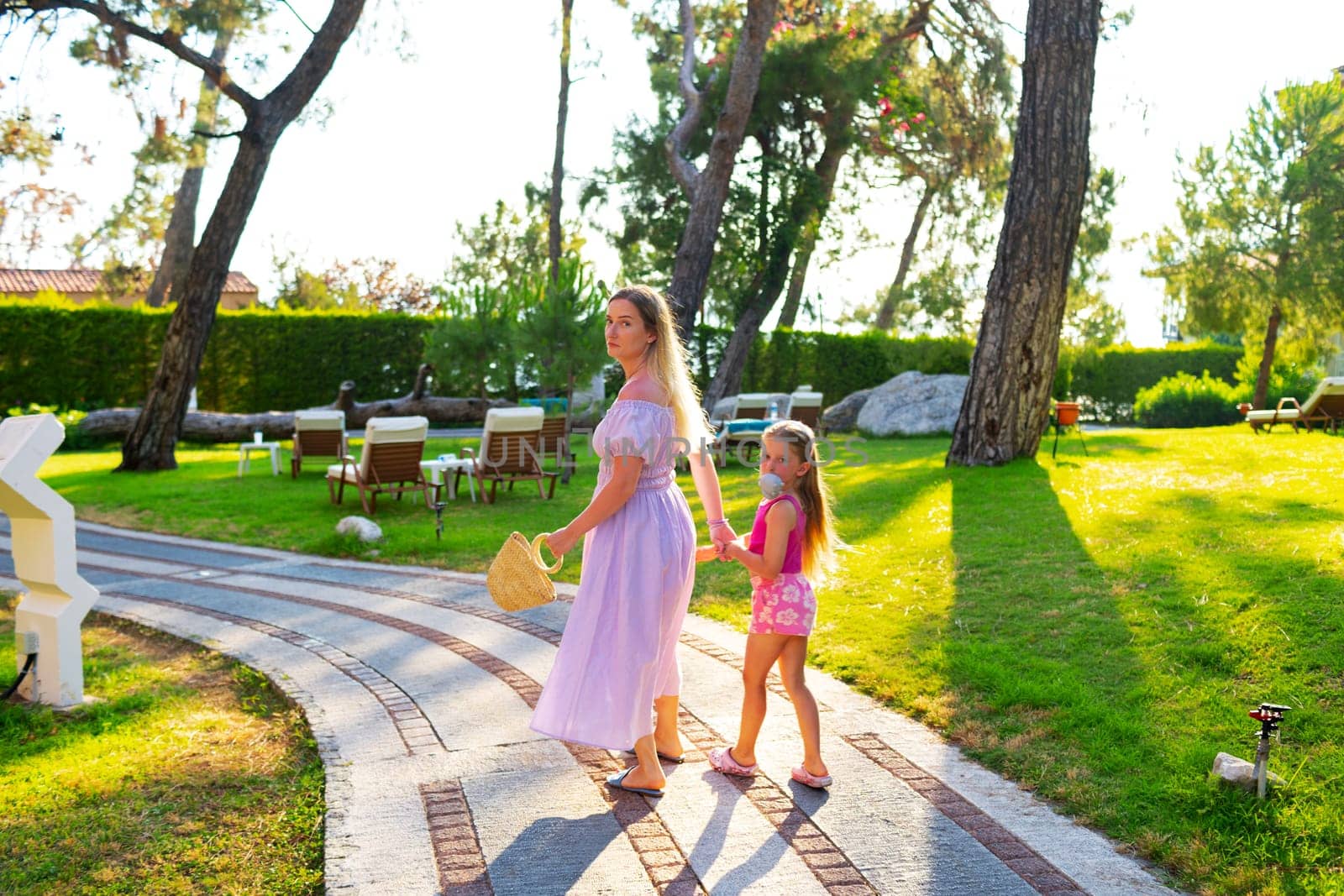 Mother and daughter enjoying walk outdoors in summer, back view