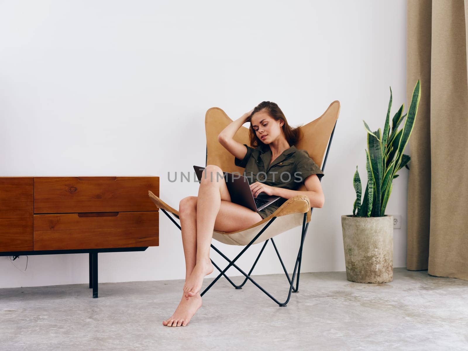 Female student study sits on a chair with a laptop work at home smile and relax, modern stylish interior Scandinavian lifestyle, copy space. by SHOTPRIME