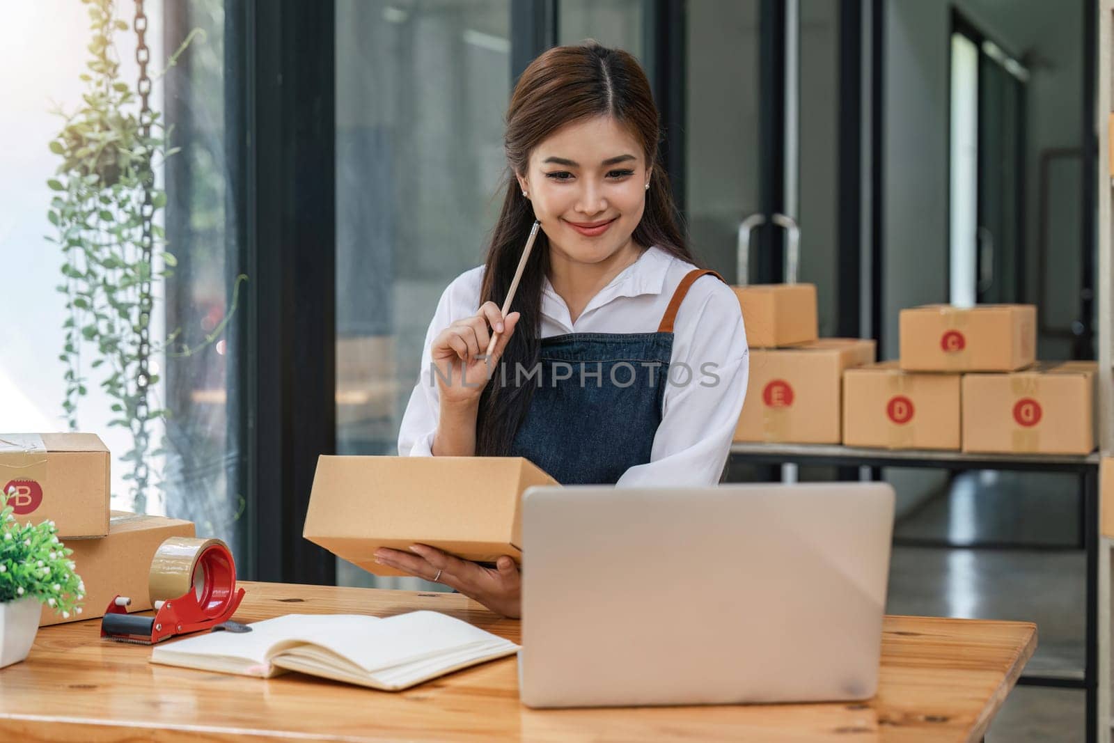 Woman who e-commerce business is writing a list of customers on paper before shipping to them, she runs an e-commerce business on websites and social media. Concept of selling products online.