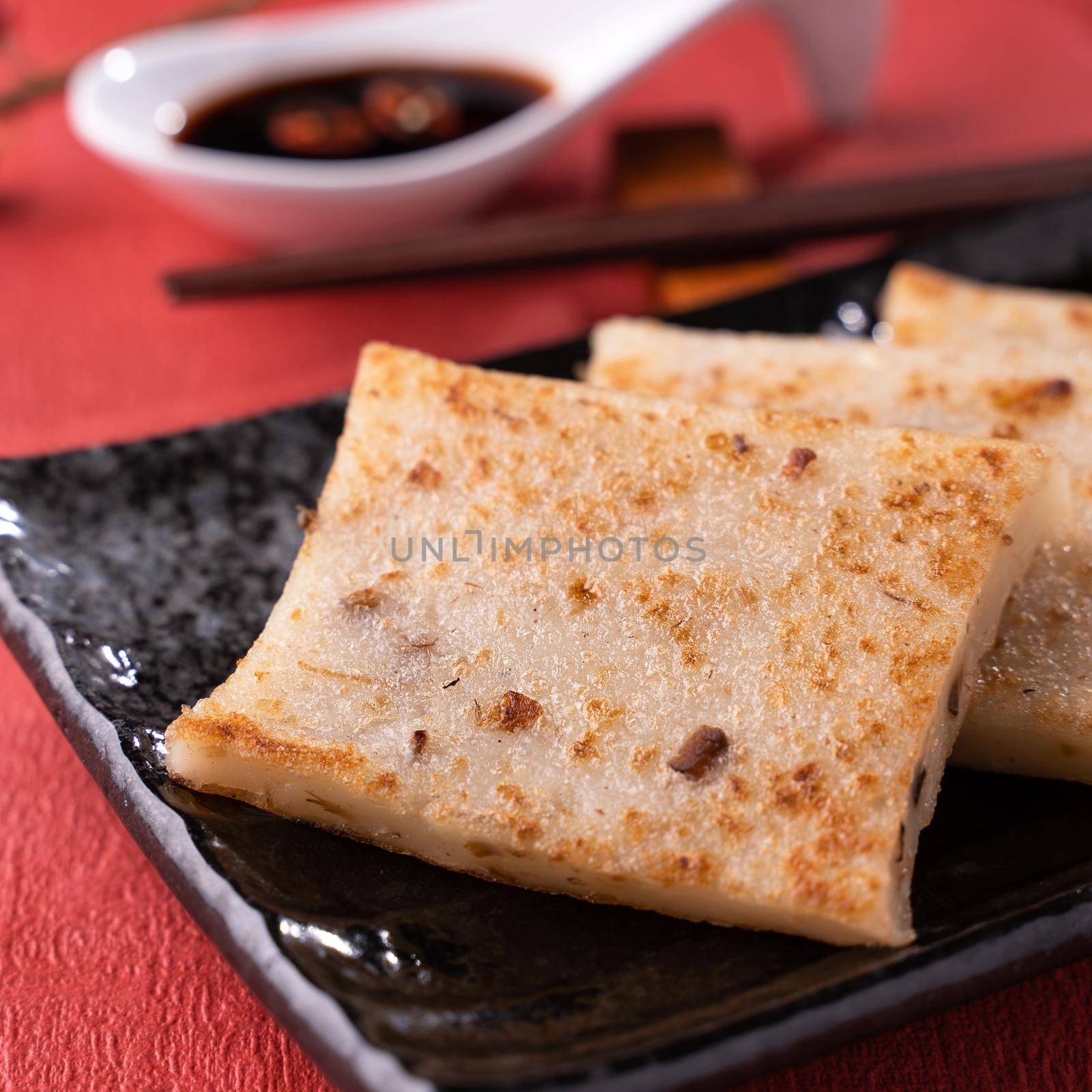 Chinese lunar new year food concept, Delicious turnip radish cake, local cuisine in restaurant with soy sauce on red background, close up, copy space