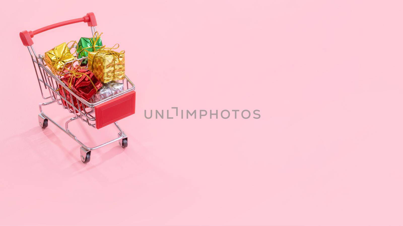 Annual sale, Christmas shopping season concept - mini red shop cart trolley full of gift box isolated on pale pink background, copy space, close up