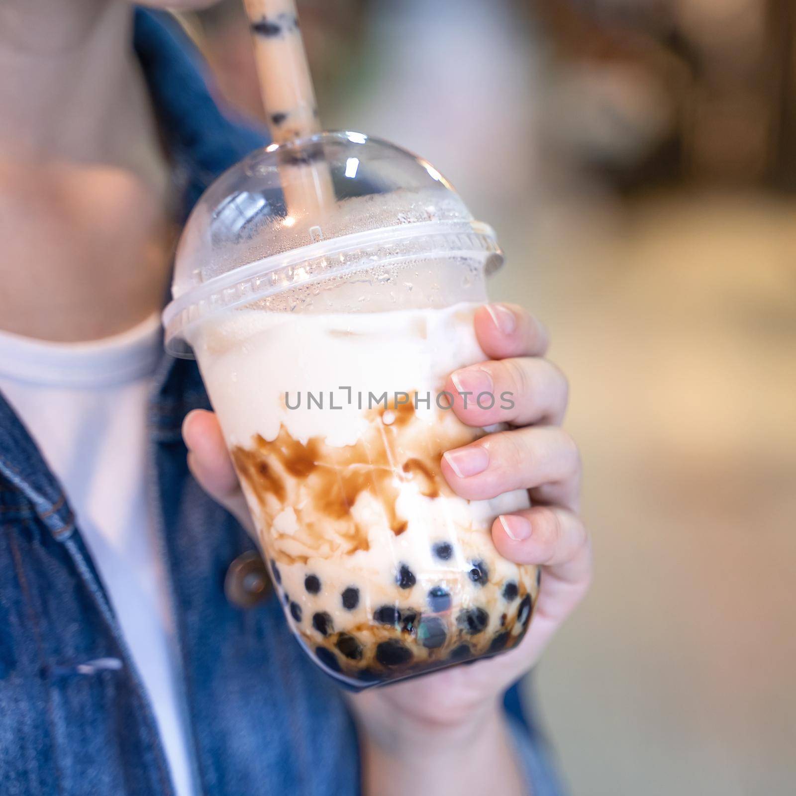 Young woman is holding, drinking brown sugar flavored tapioca pearl bubble milk tea with glass straw in night market of Taiwan, close up, bokeh by ROMIXIMAGE