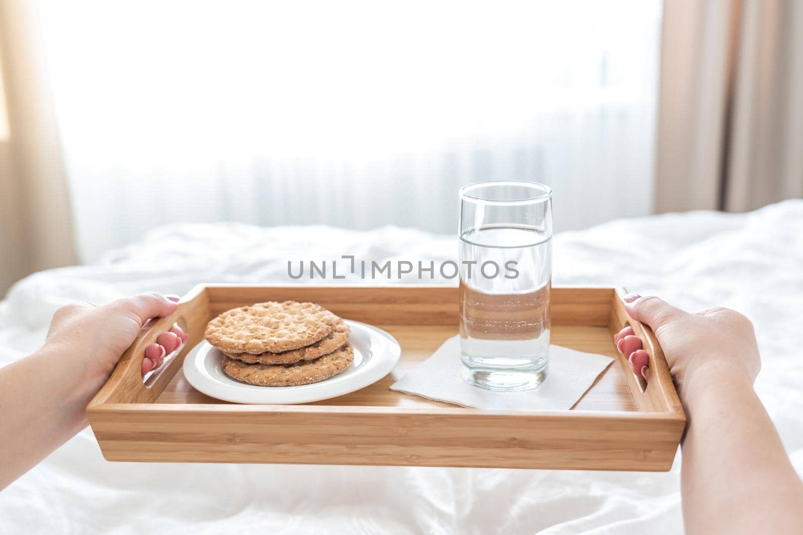 Woman holding tray with diet breakfast of crackers and water on bed