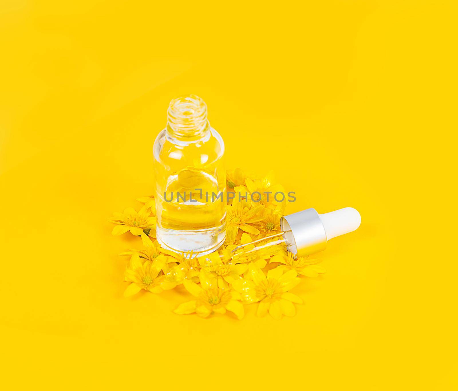 A bottle with a pipette serum on a yellow background surrounded by spring flowers