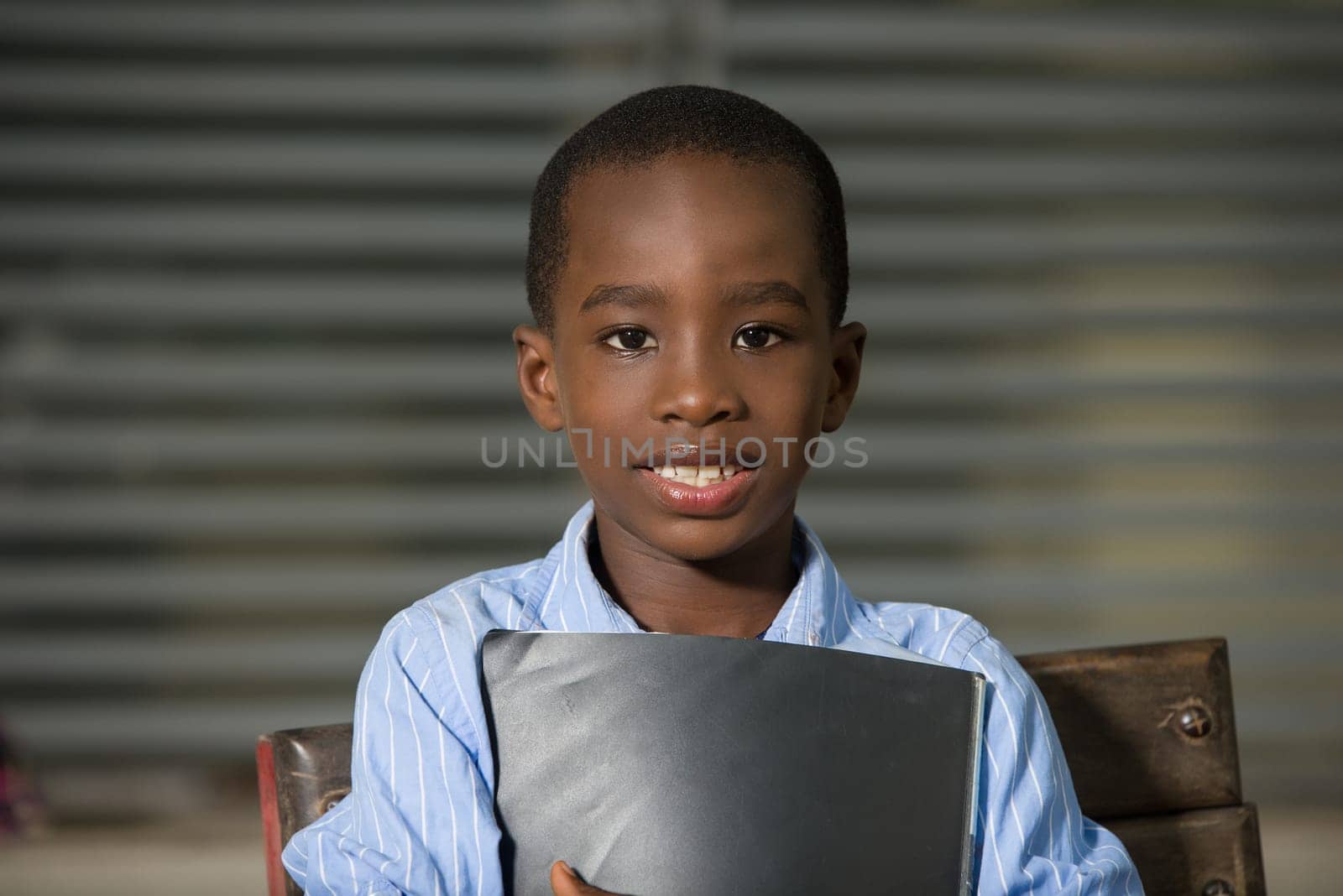 Happy satisfied child carrying in primary school. Close Up African schoolboy face standing outside.
