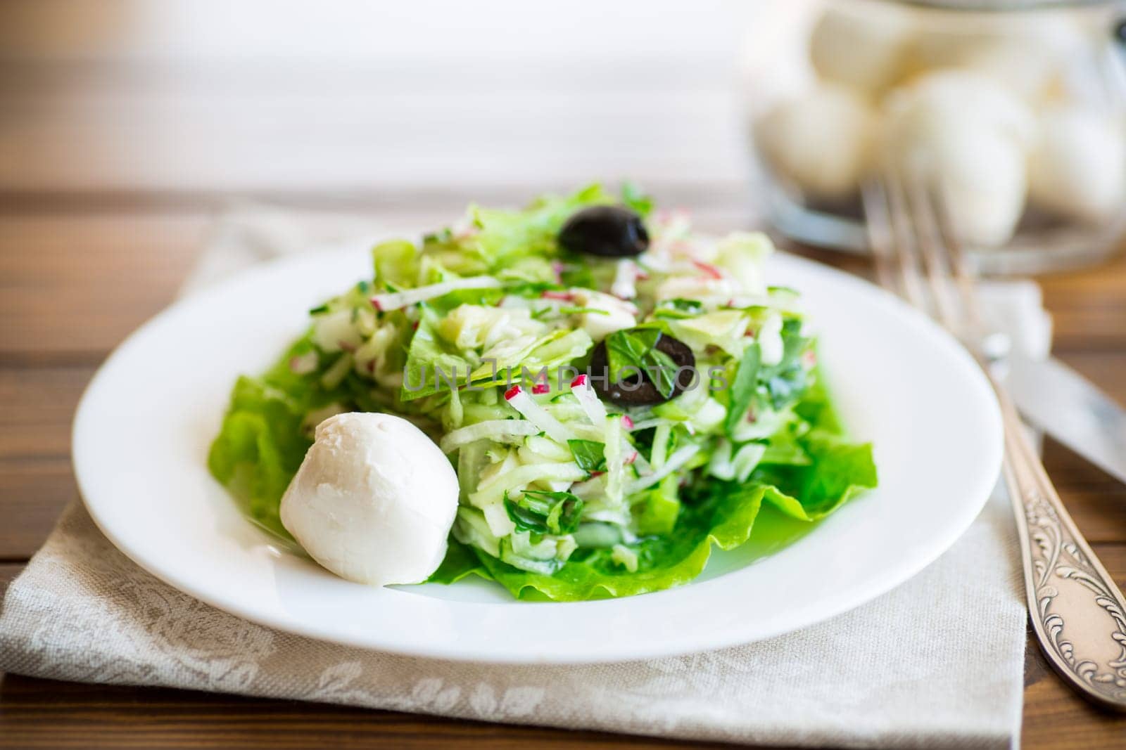 fresh summer salad with early cabbage, cucumbers, radishes and other vegetables in a plate on a wooden table.