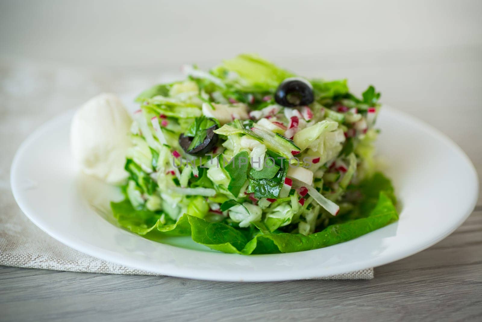 fresh summer salad with early cabbage, cucumbers, radishes and other vegetables in a plate on a wooden table.