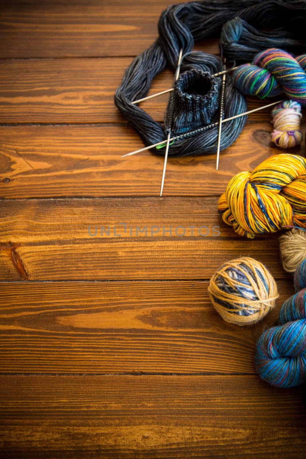 Colored threads, knitting needles and other items for hand knitting, on a dark wooden table .
