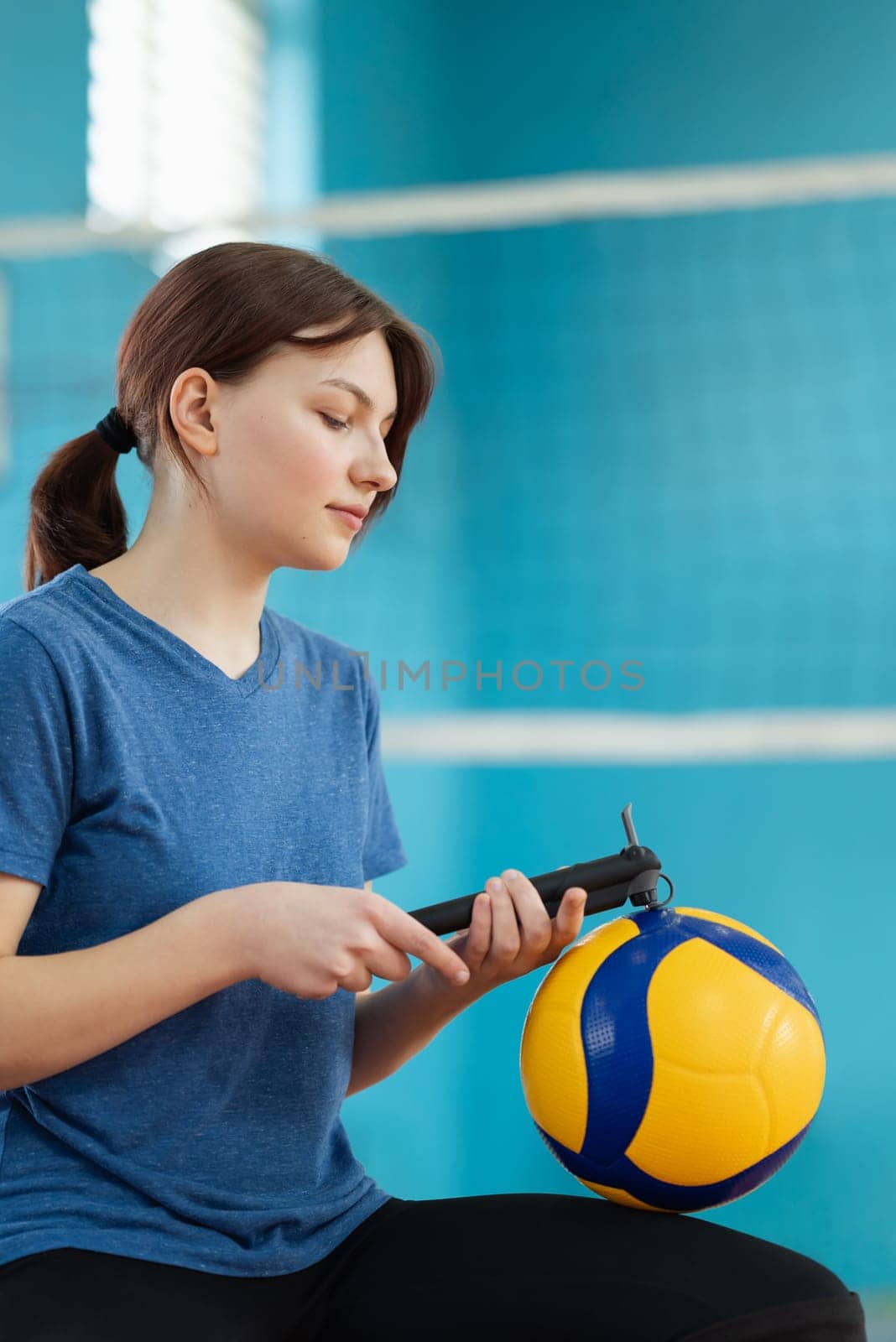 Young girl inflating new volleyball ball with small hand pump in gymnasium by VitaliiPetrushenko