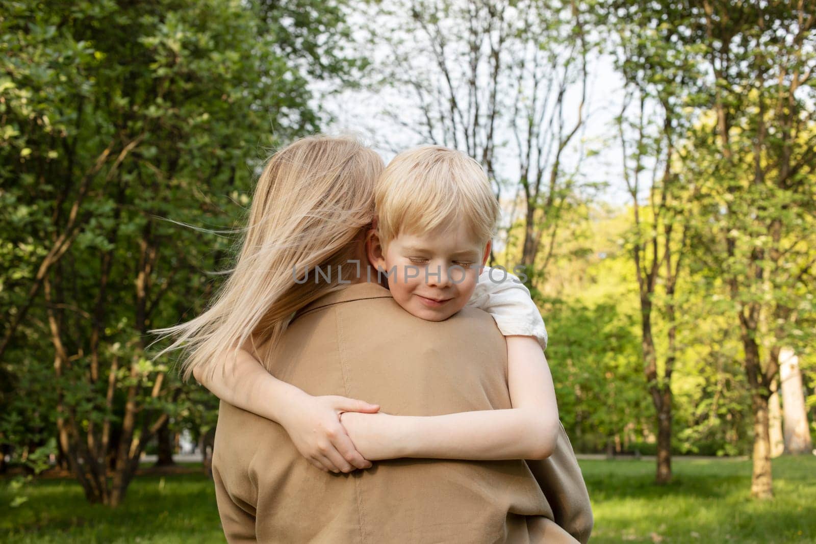 Little Smiling Caucasian 7 Yo Boy Sits In Mother's Arms, Hugging Her Tight. Mom's Support And Care. Summer Time. Parenthood, Family Leisure Time. Children's Day. Horizontal Plane.