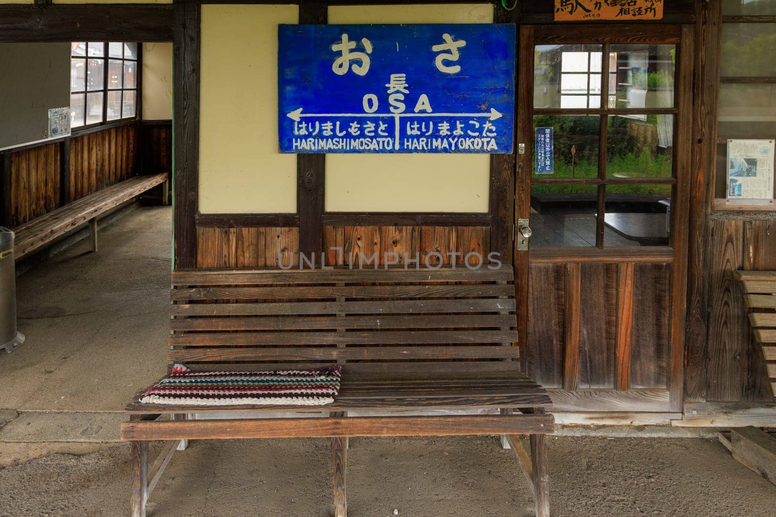 Hyogo, Japan - May 15, 2023: Empty bench and waiting room with sign for Osa Station in rural area by Osaze