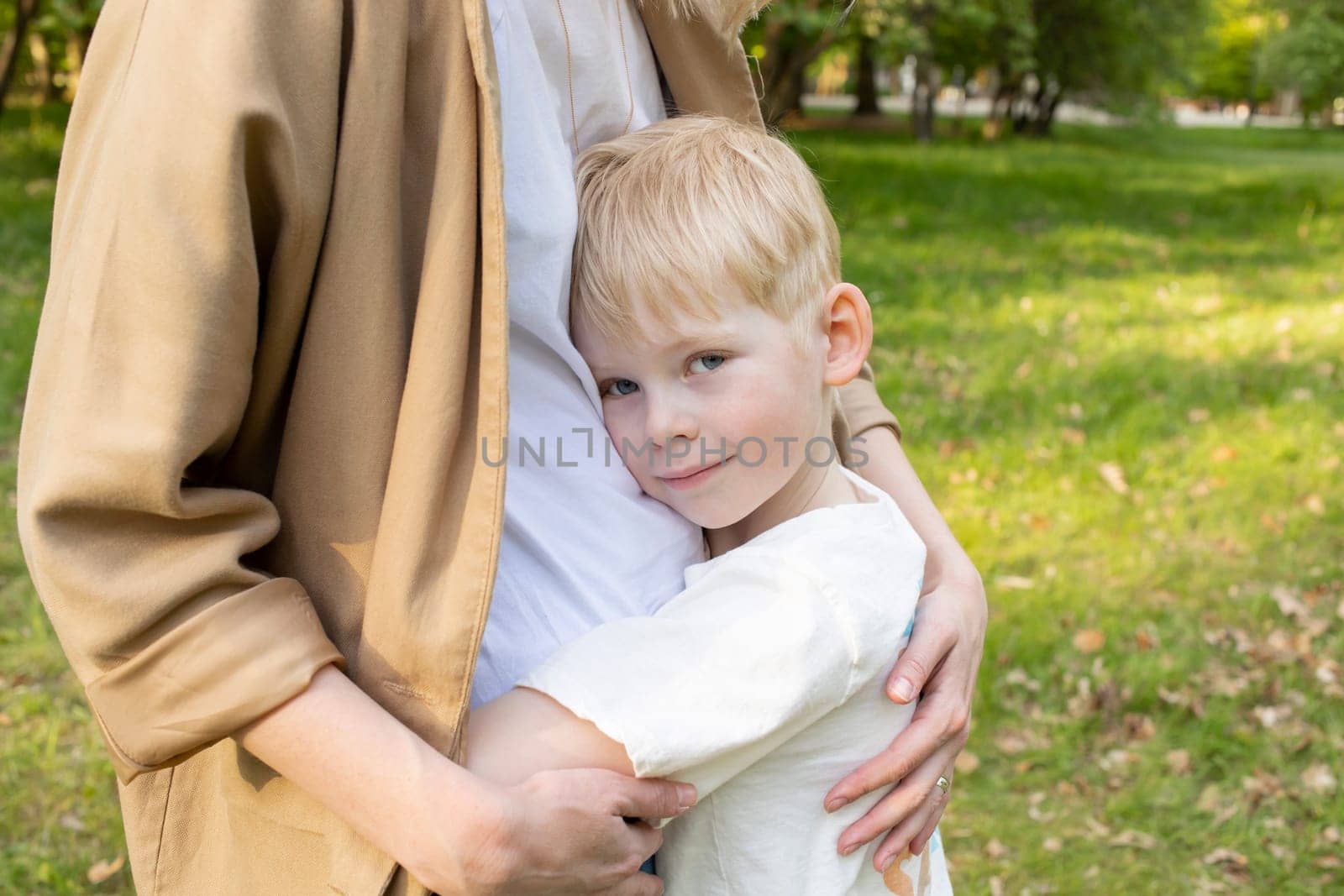 Little Smiling Caucasian 7 Yo Boy Hugs His Mother Tight in Park. Mom's Support And Care. Summer Time. Motherhood, Family Leisure Time. Children's Day. Horizontal Plane. High quality photo