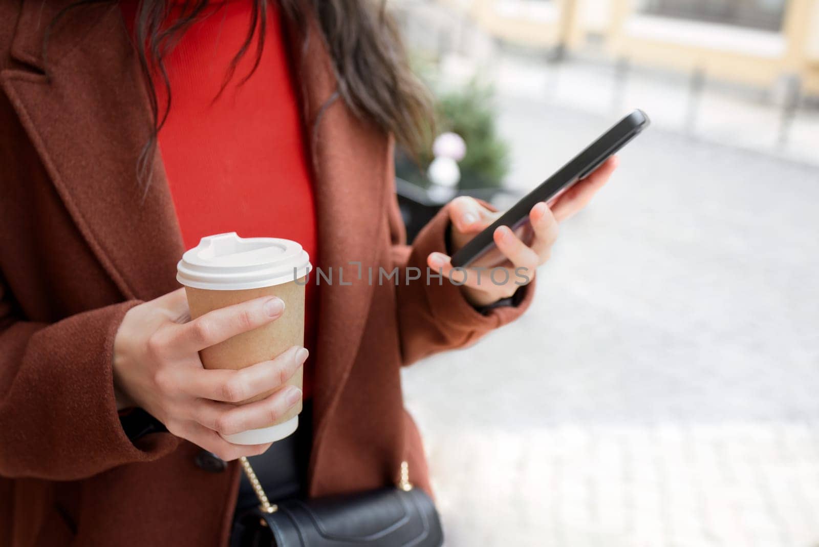Woman uses mobile phone on the street and sips coffee.