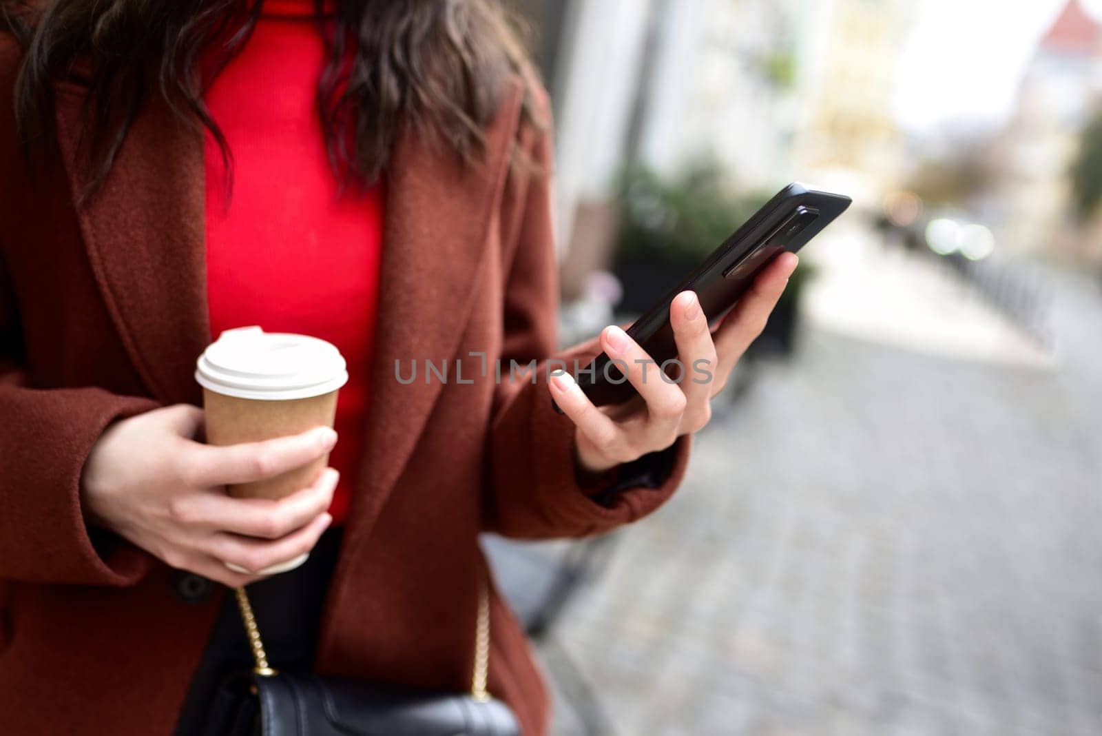 cropped woman's hands holding smart phone with cup of coffee. by Nickstock