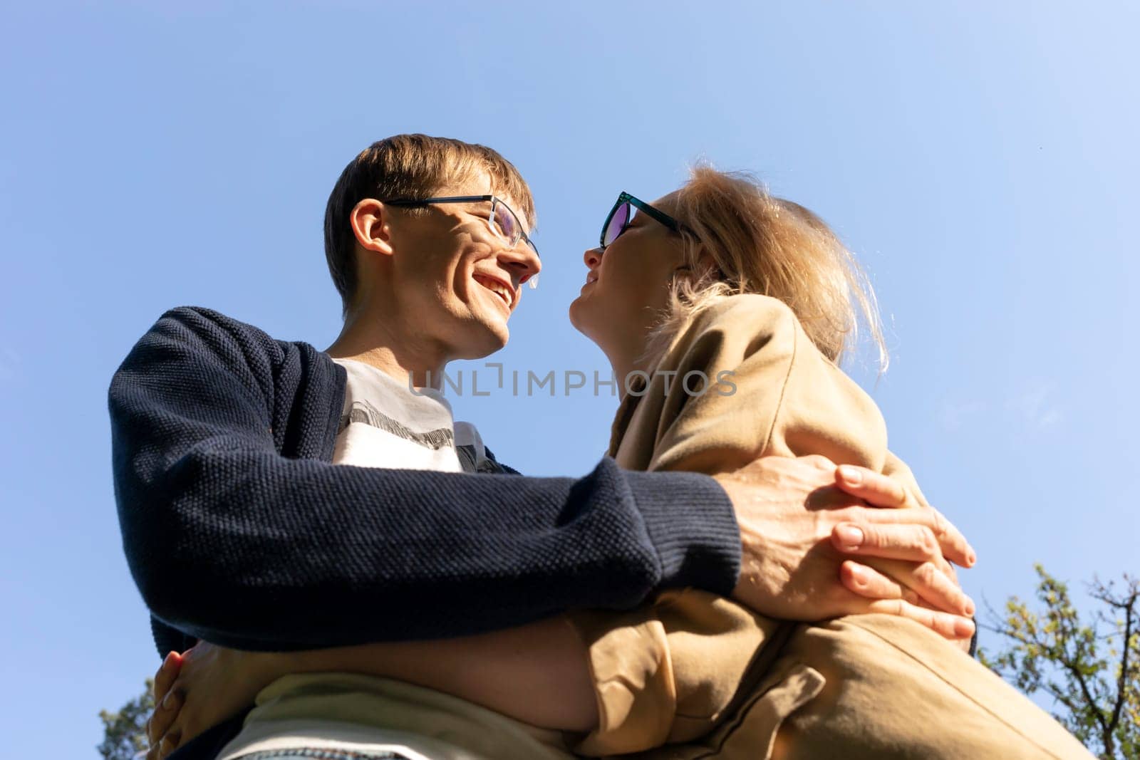 Hugging Happy Smiling Couple Looking At Eyes Of One Another, Blue Sky On Background. Relationship, Togetherness. Enjoying Time Together. Feelings. Vertical Plane Summer Time. High quality photo