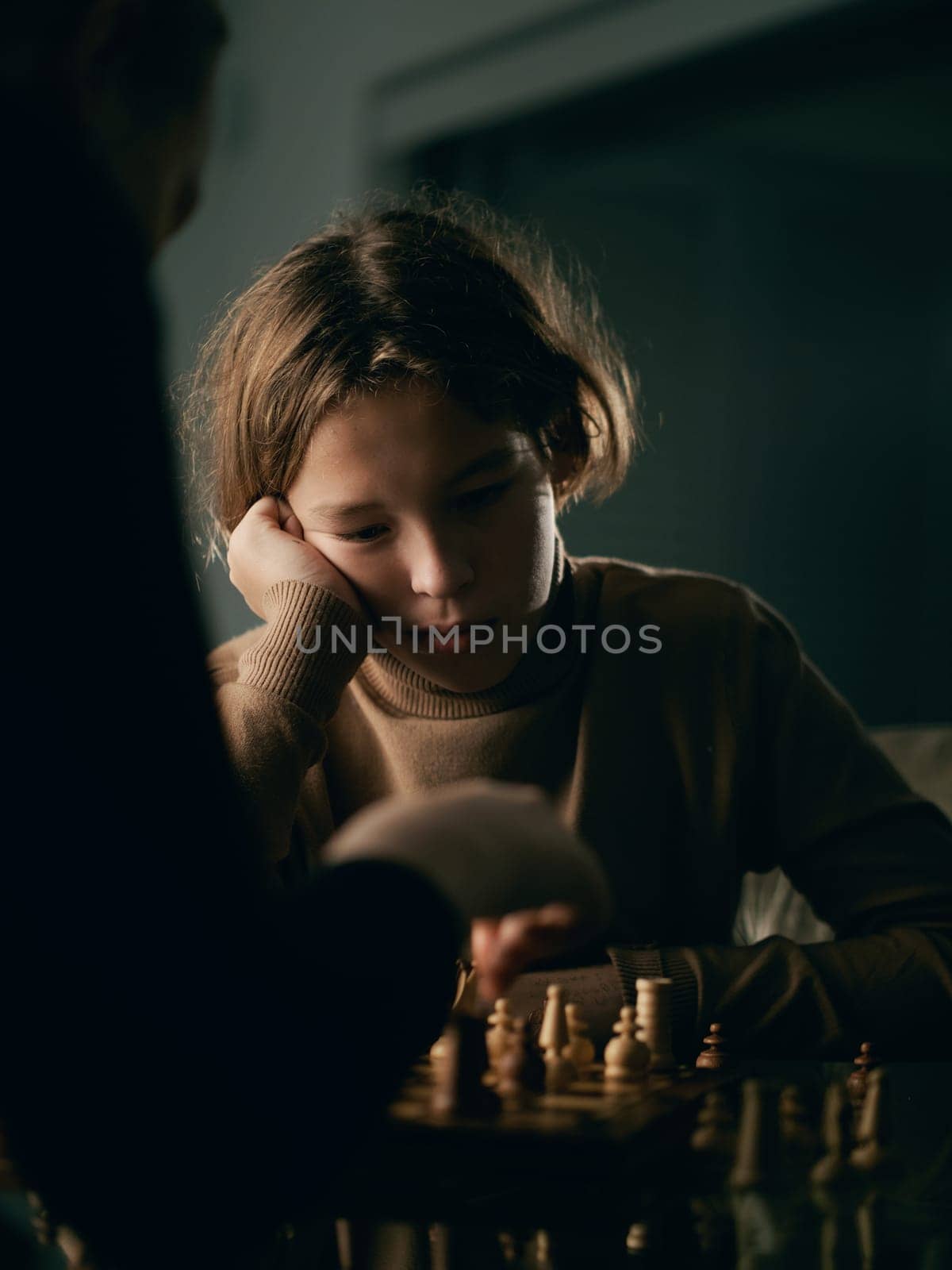 Vertical photo of teenager 12 years old plays chess at home in the evening