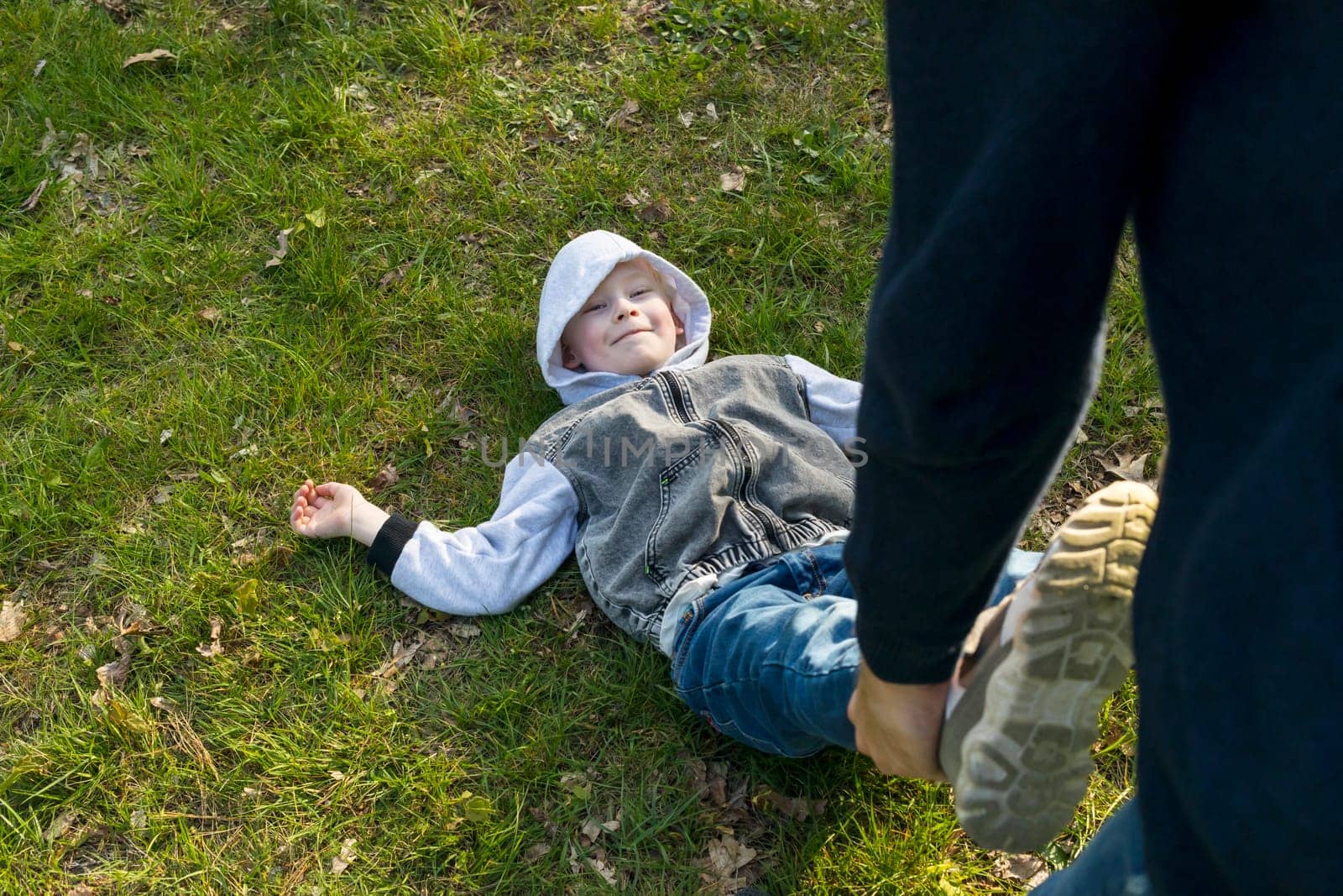 White Father Plays With Child In Meadow, Happy Smiling Boy Lying On Grass. Summer Time. Father's Day, Family Leisure Time, Playing Games. Emotional Connection, Love And Care. Horizontal Plane.