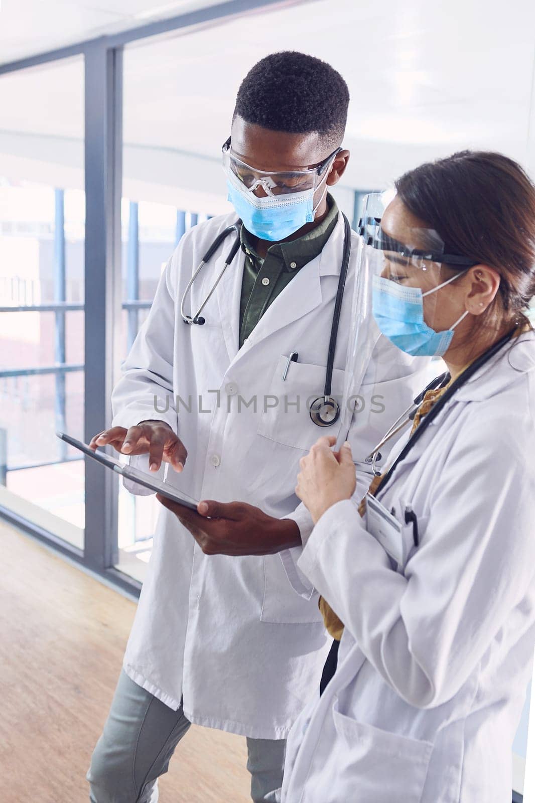 Using technology to stay ahead of the curve. two young doctors working on a digital tablet while standing in the hospital. by YuriArcurs