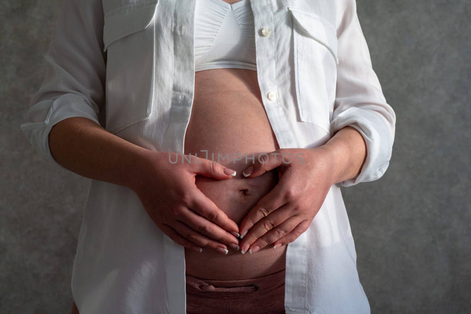 Belly of a pregnant woman. Pregnancy concept. Woman holding hands in heart shape by Mariakray