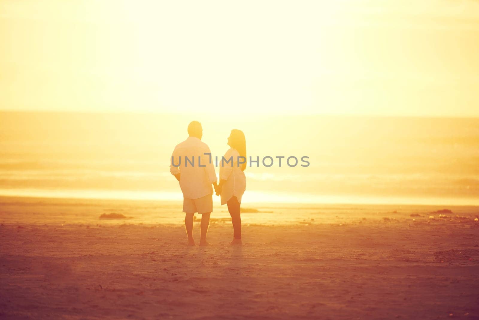 Keeping the romance alive. Rearview shot of an affectionate mature couple walking hand in hand on the beach. by YuriArcurs