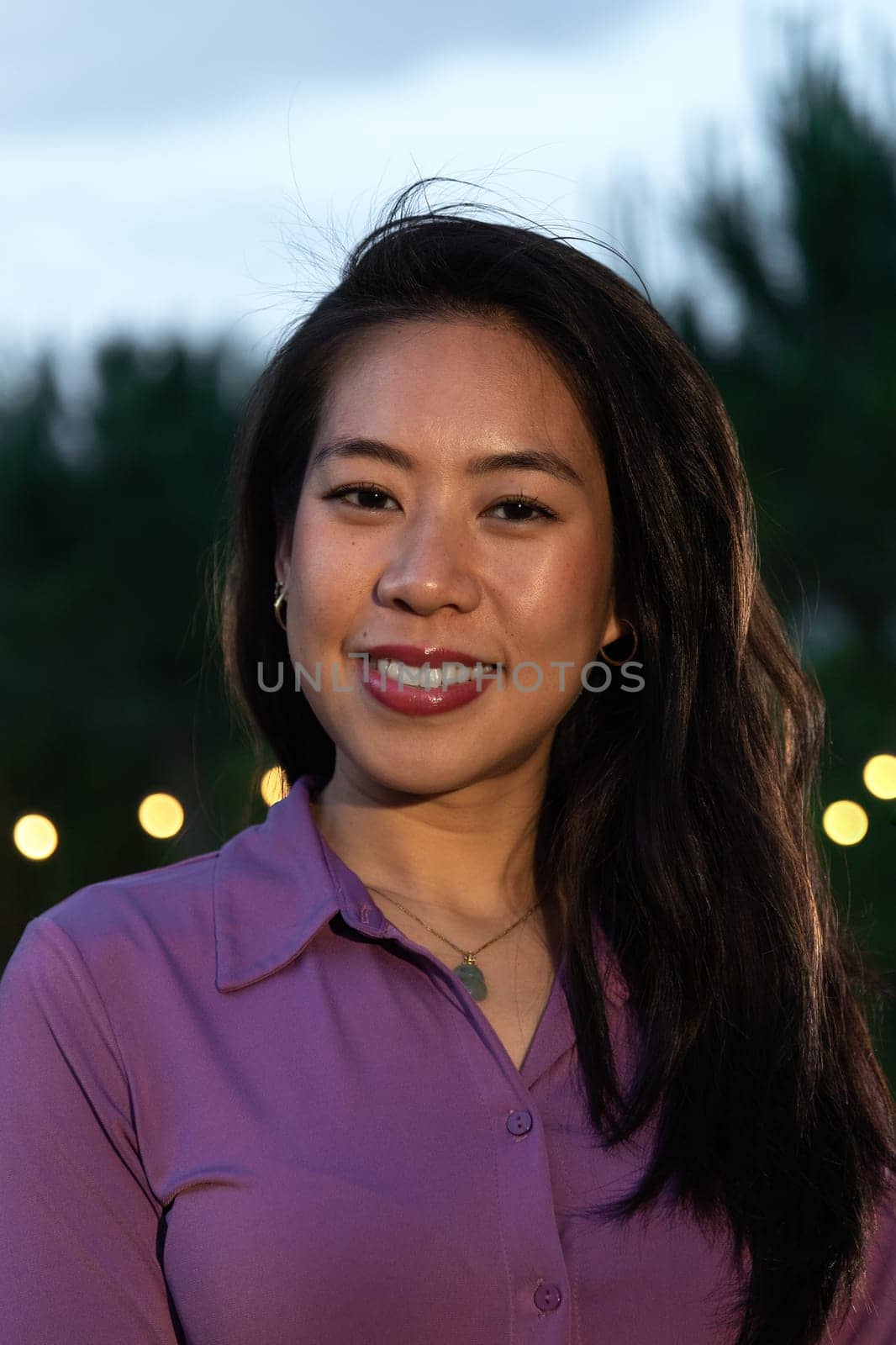 Vertical headshot of young smiling asian woman at sunset. Lifestyle.