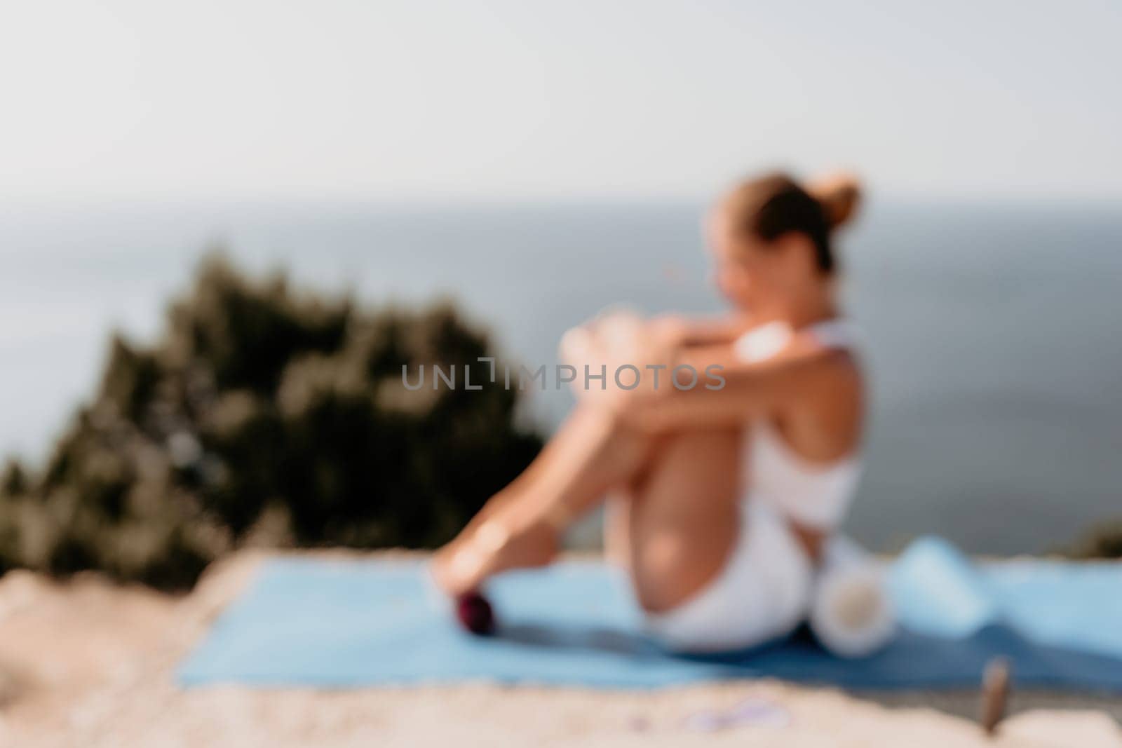 Abstract defocused fitness woman sea. A happy middle aged woman in white sportswear exercises morning outdoors in a park with a beach view. Female fitness pilates yoga routine concept. Healthy lifestyle. by panophotograph