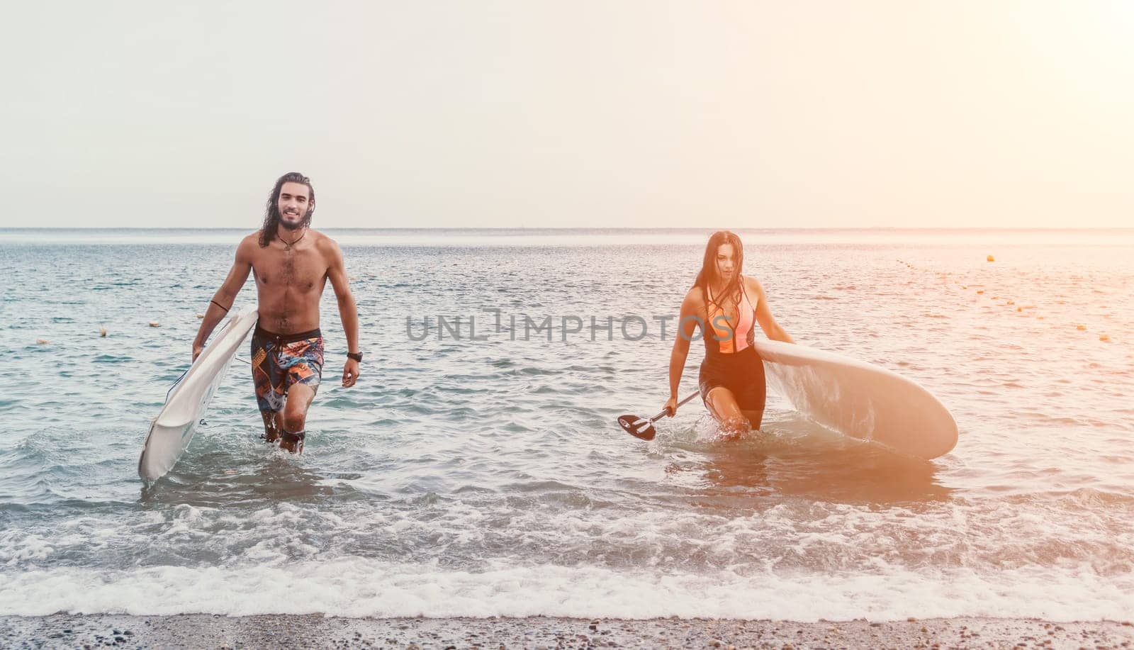 Sea woman and man on sup. Silhouette of happy young woman and man, surfing on SUP board, confident paddling through water surface. Idyllic sunset. Active lifestyle at sea or river