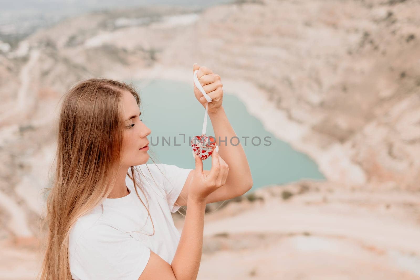 Woman travel portrait. Happy woman with long hair looking at camera and smiling. Close up portrait cute woman is posing on a heart shaped lake - travel destination by panophotograph