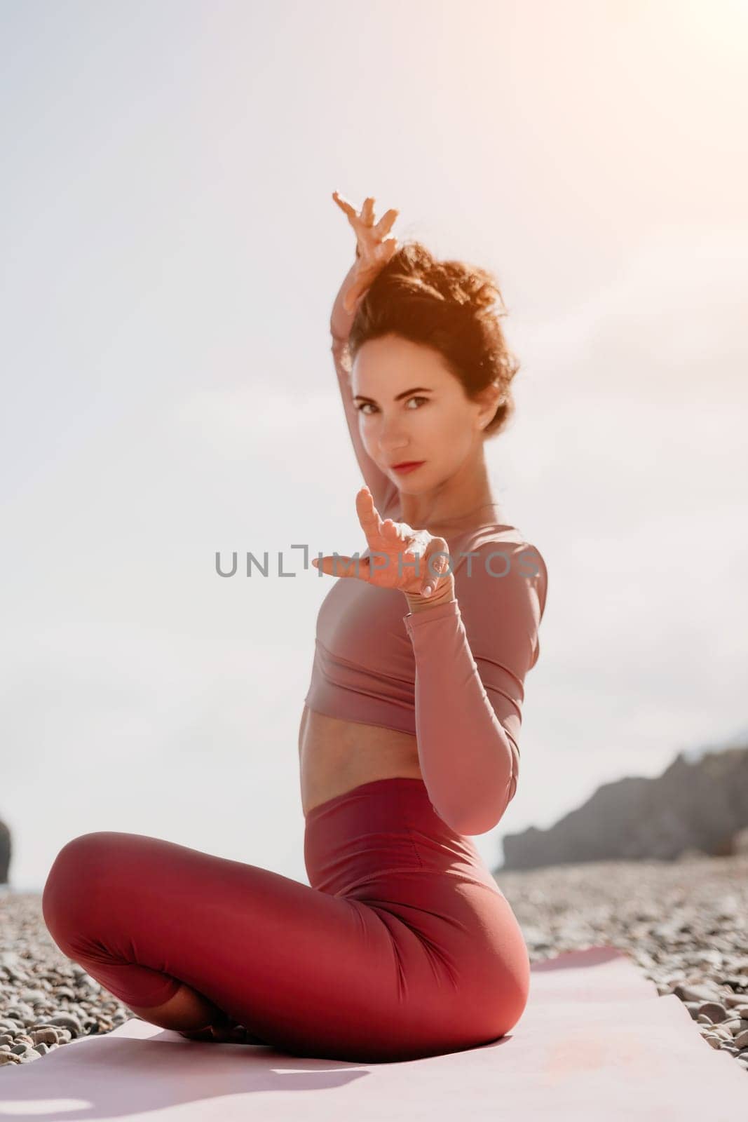 Young woman with long hair in white swimsuit and boho style braclets practicing outdoors on yoga mat by the sea on a sunset. Women's yoga fitness routine. Healthy lifestyle, harmony and meditation