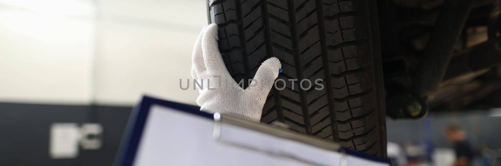 Auto mechanic technician holds blank clipboard sheet in hand with copy space text and car tires by kuprevich