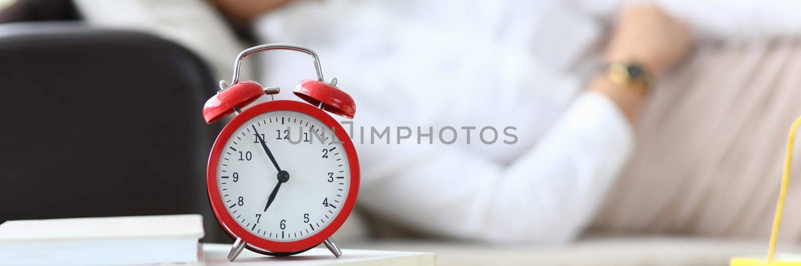 Alarm clock at seven o'clock and woman sleeping on couch. Fatigue and restful sleep concept