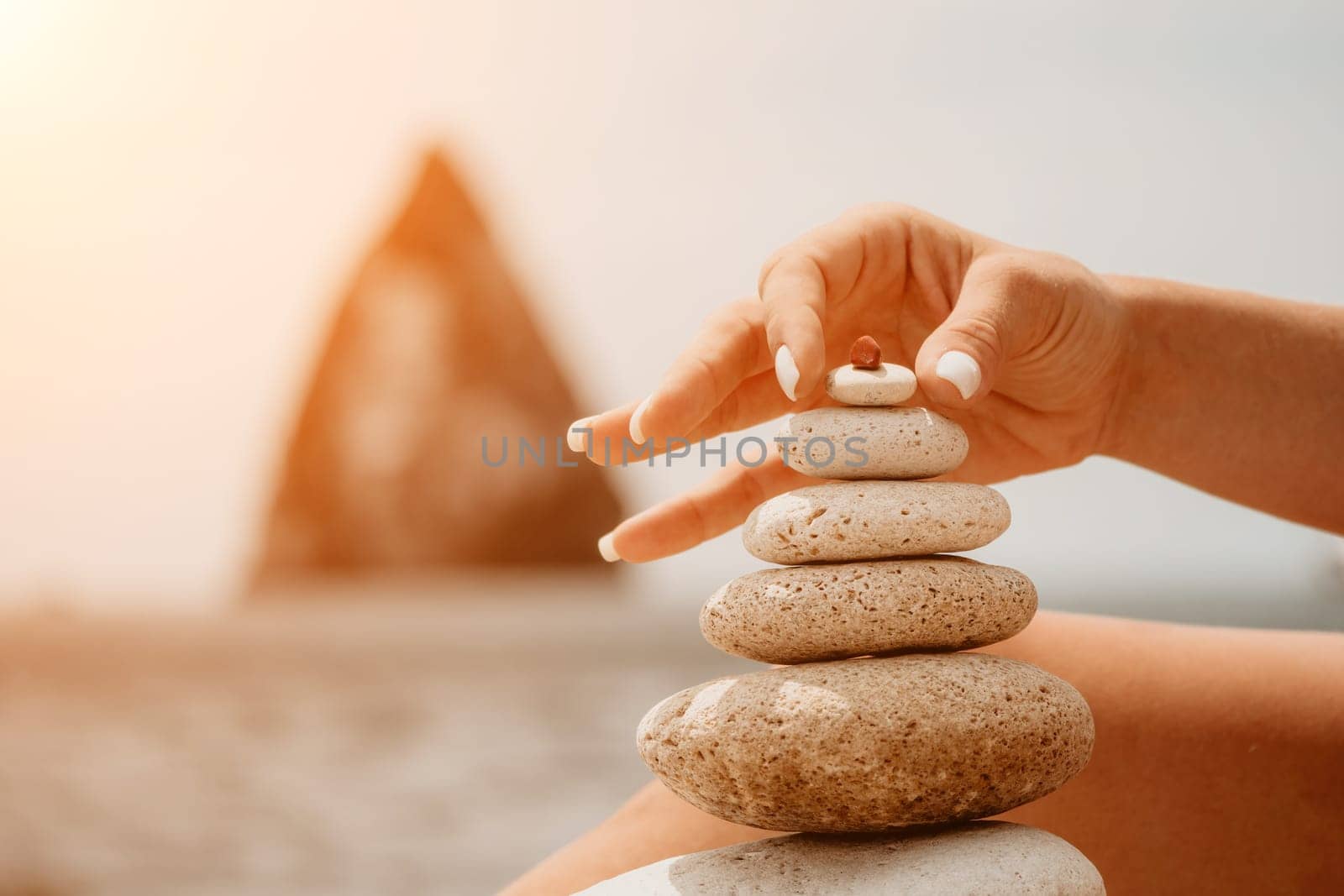 Woman bilds stones pyramid on the seashore on a sunny day on the blue sea background. Happy holidays. Pebble beach, calm sea, travel destination. Concept of happy vacation on the sea, meditation, spa