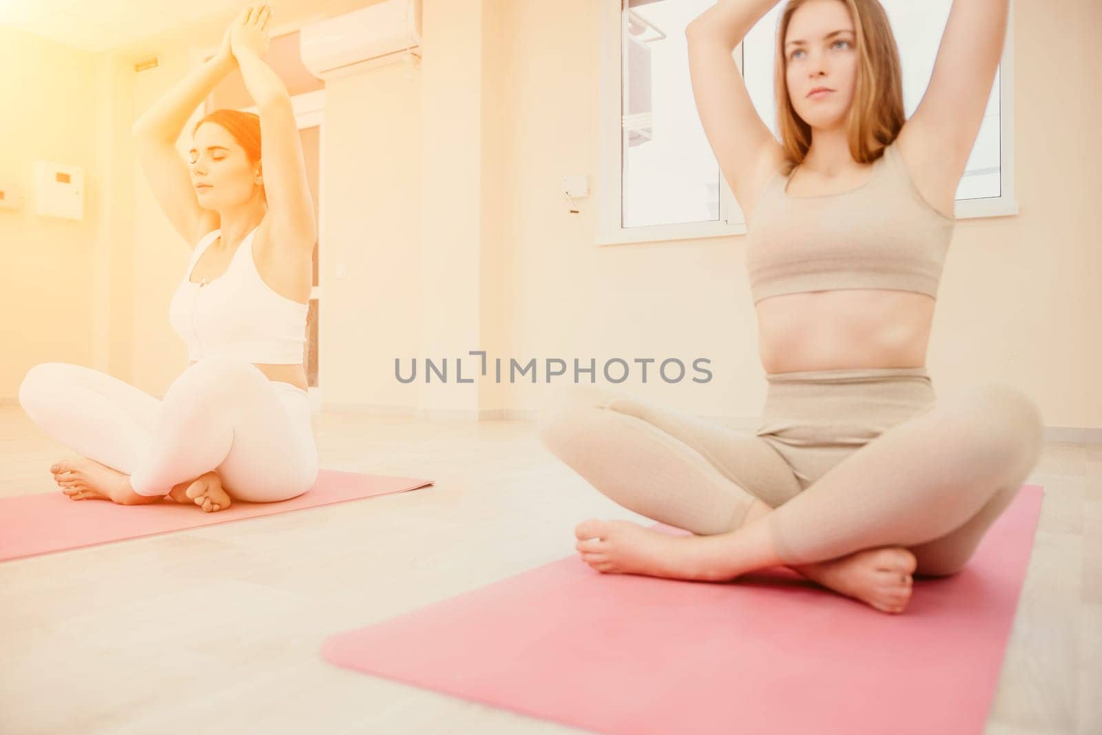 Group of young womans fitness instructor in Sportswear Leggings and Tops, stretching in the gym before pilates, on a yoga mat near the large window on a sunny day, female fitness yoga routine concept.