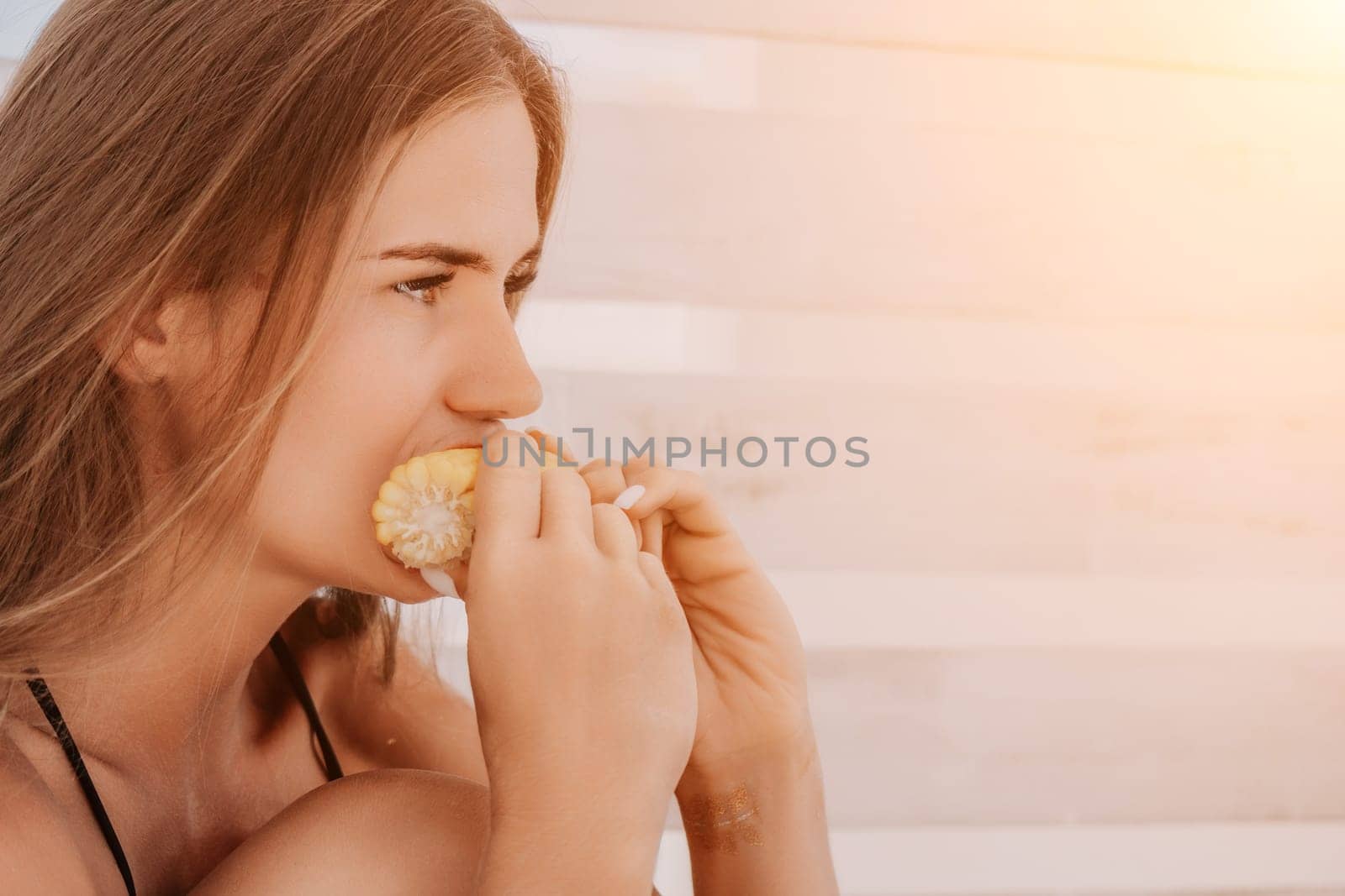 Healthy vegetarian hipster woman in summer outfit eat grilled corn and look to camera. Sexy lady on sea beach sunset or ocean sunrise. Travel, explore, active yoga and meditation lifestyle concept.