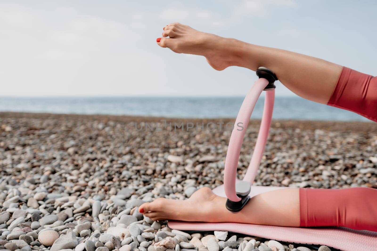 Woman sea pilates. Sporty happy middle aged woman practicing fitness on beach near sea, smiling active female training with ring on yoga mat outside, enjoying healthy lifestyle, harmony and meditation by panophotograph