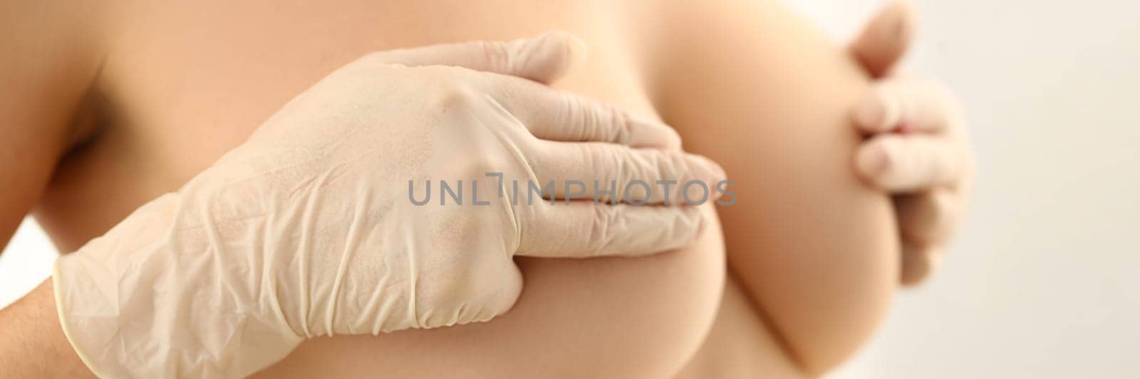 Woman with naked beautiful breasts closes nipples with gloved hands. Breast medical examination and mammologist concept