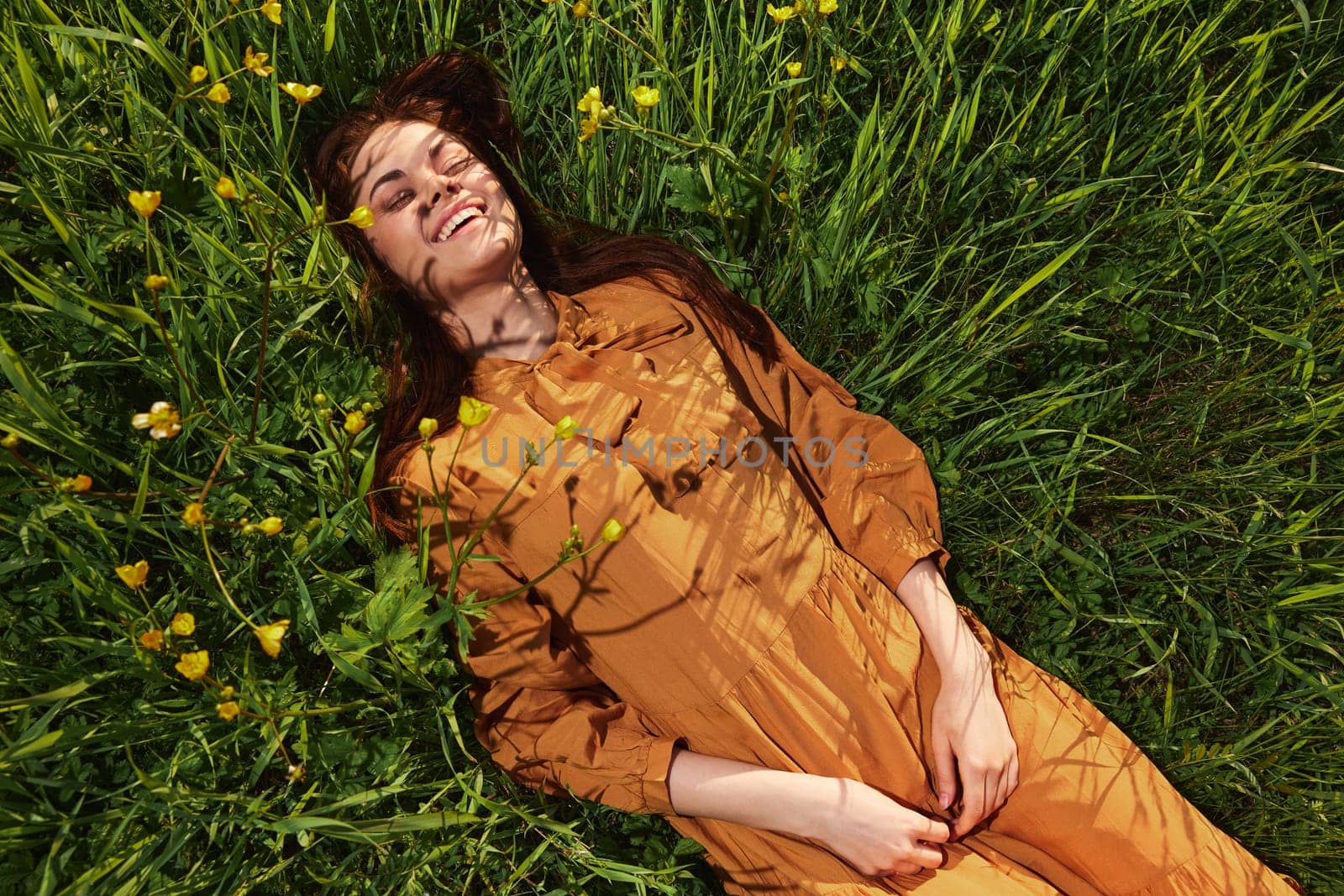 a calm woman with long red hair lies in a green field with yellow flowers, in an orange dress with her eyes closed, with a pleasant smile on her face, enjoying peace and recuperating by Vichizh