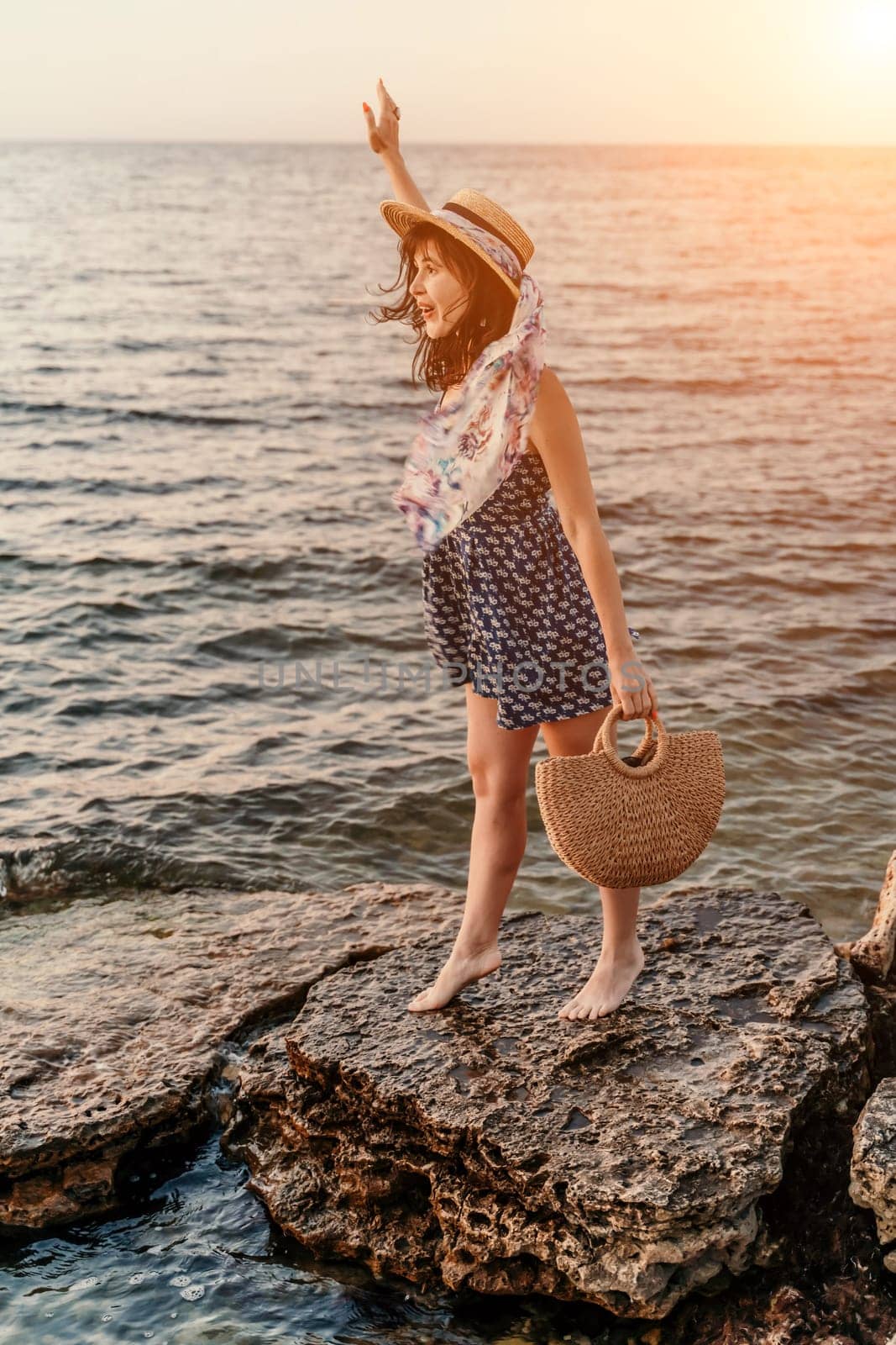 A woman in a dress, hat and with a straw bag is standing on the beach enjoying the sea. Happy summer holidays by Matiunina