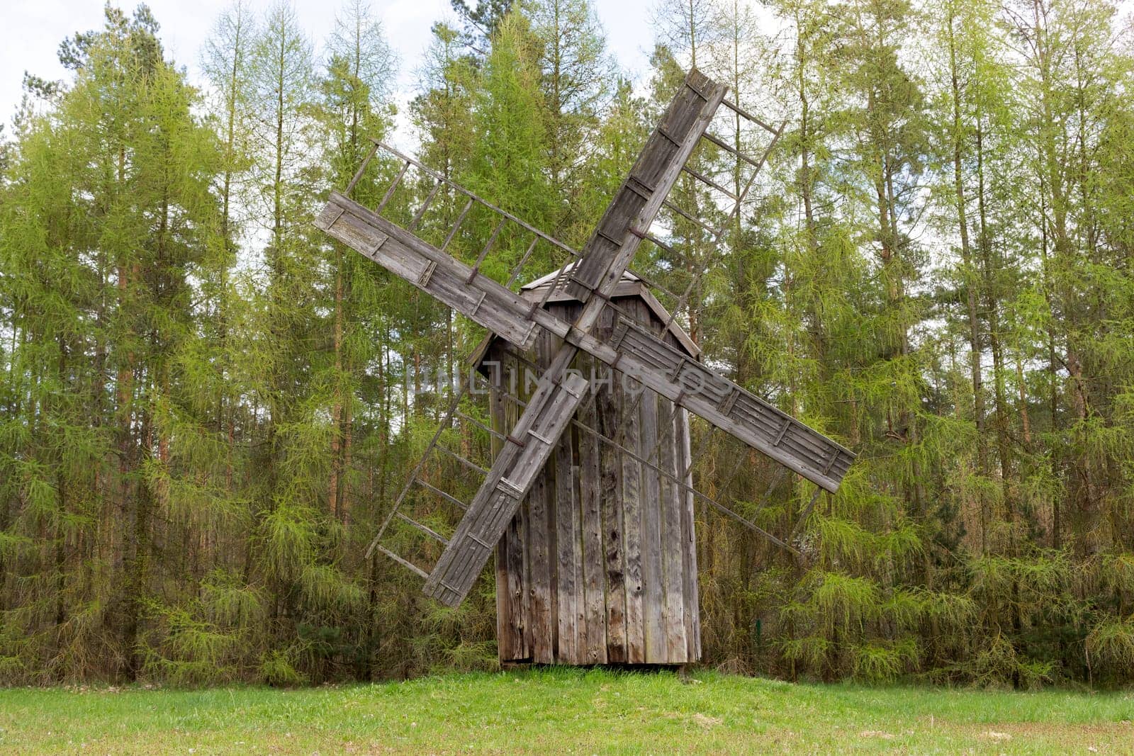 Old Wooden Windmill In Meadow, Open Air. Blades Of Mill Wooden In Rural Eastern Europe Area, Countryside. Green Forest On Background. Horizontal Landscape Plane High Quality Photo.