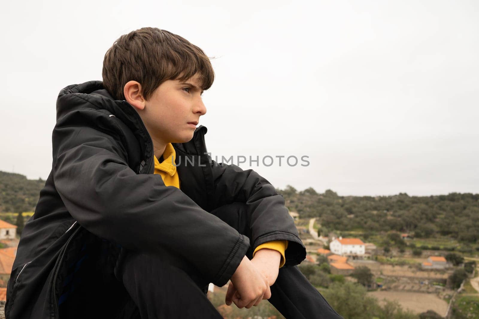 Profile of a serious young boy contemplating sitting in the mountain near a town.