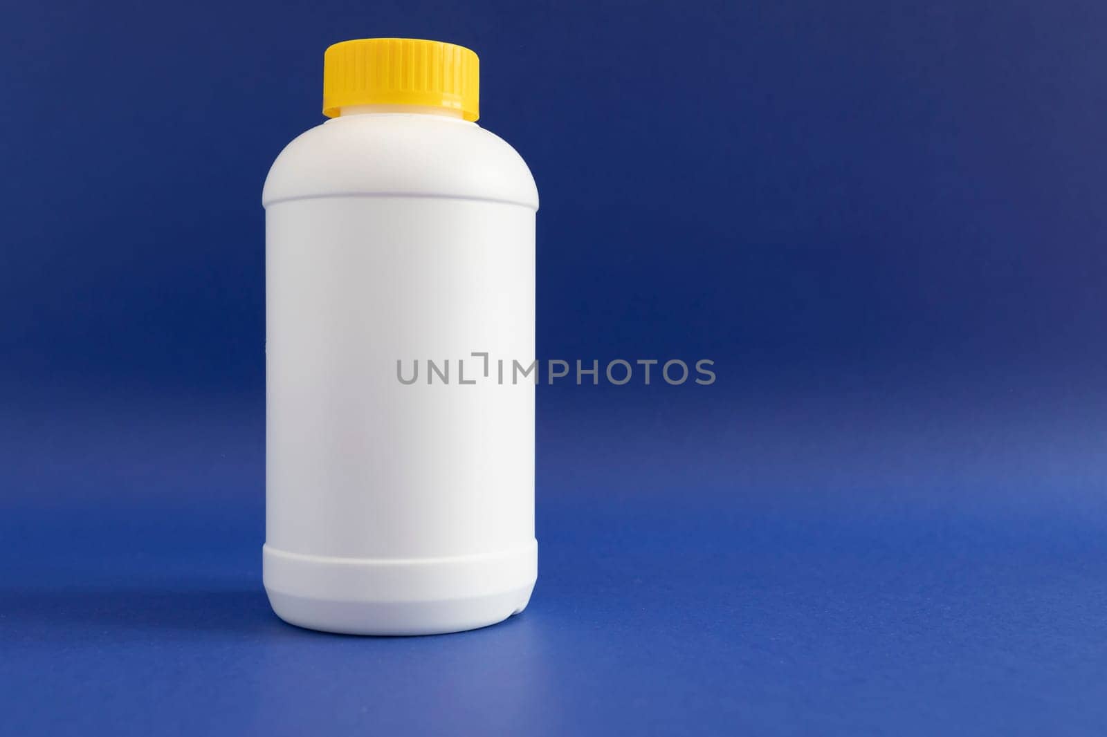 Pipe Unclogging Granules In Yellow Cap, White Plastic Bottle On Blue Purple Background. Acid Drain Cleaner, Housework Help. Horizontal Plane, Copy Space For Text.