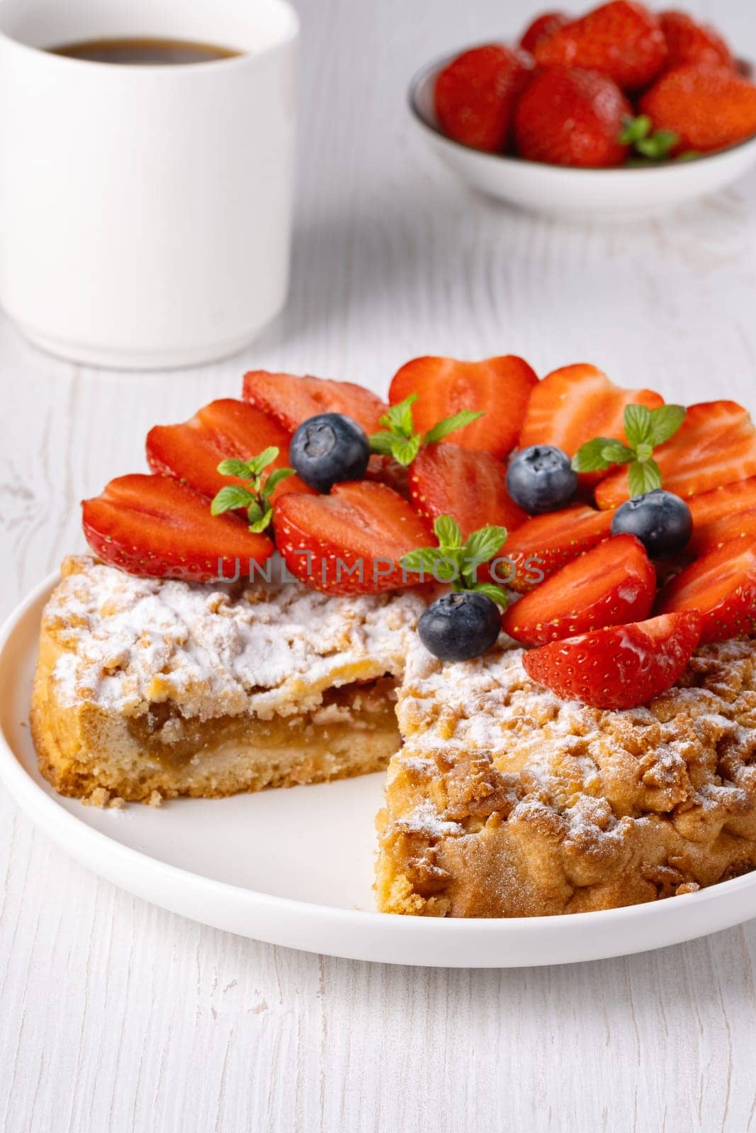 Sweet cake with strawberries on plate on white wooden background.