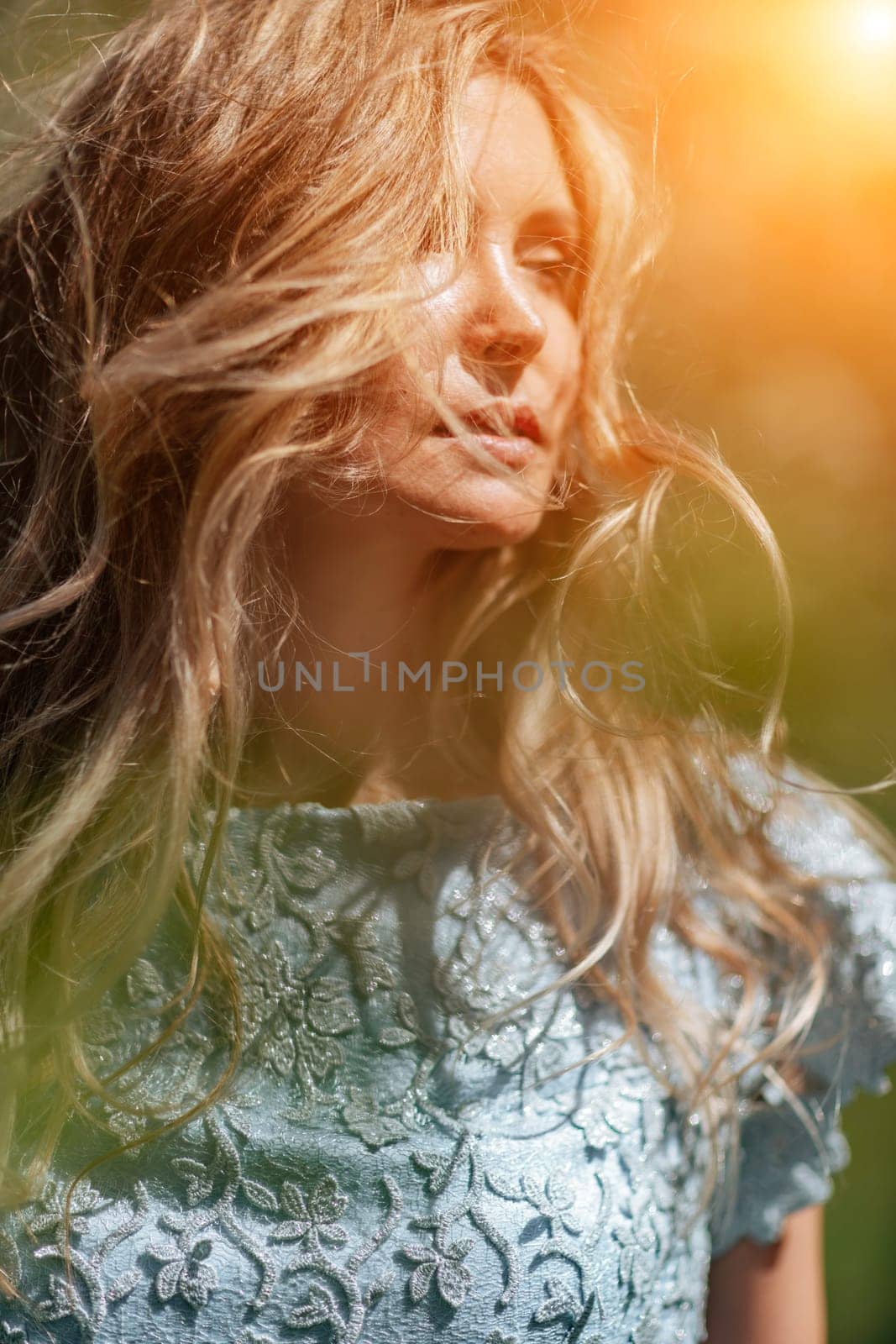 Portrait of a blonde in the park. Happy woman with long blond hair in a blue dress