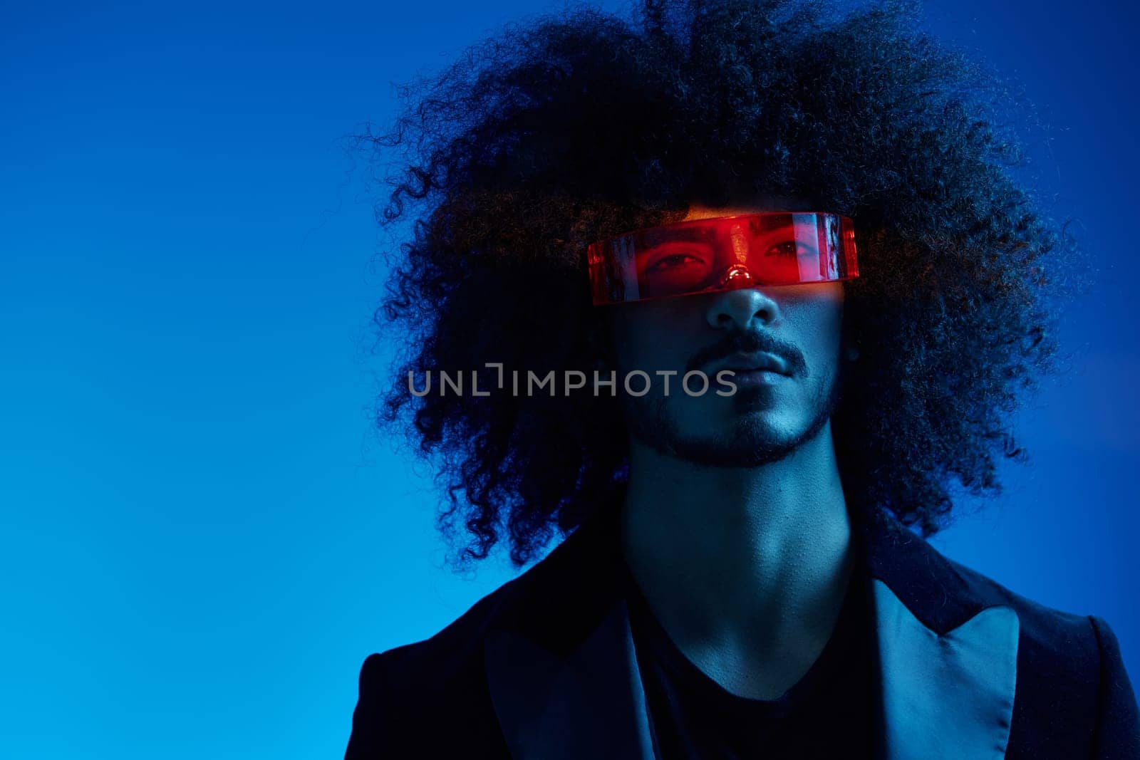 Fashion portrait of a man with curly hair on a blue background wearing red sunglasses, multinational, colored light, trendy, modern concept. High quality photo