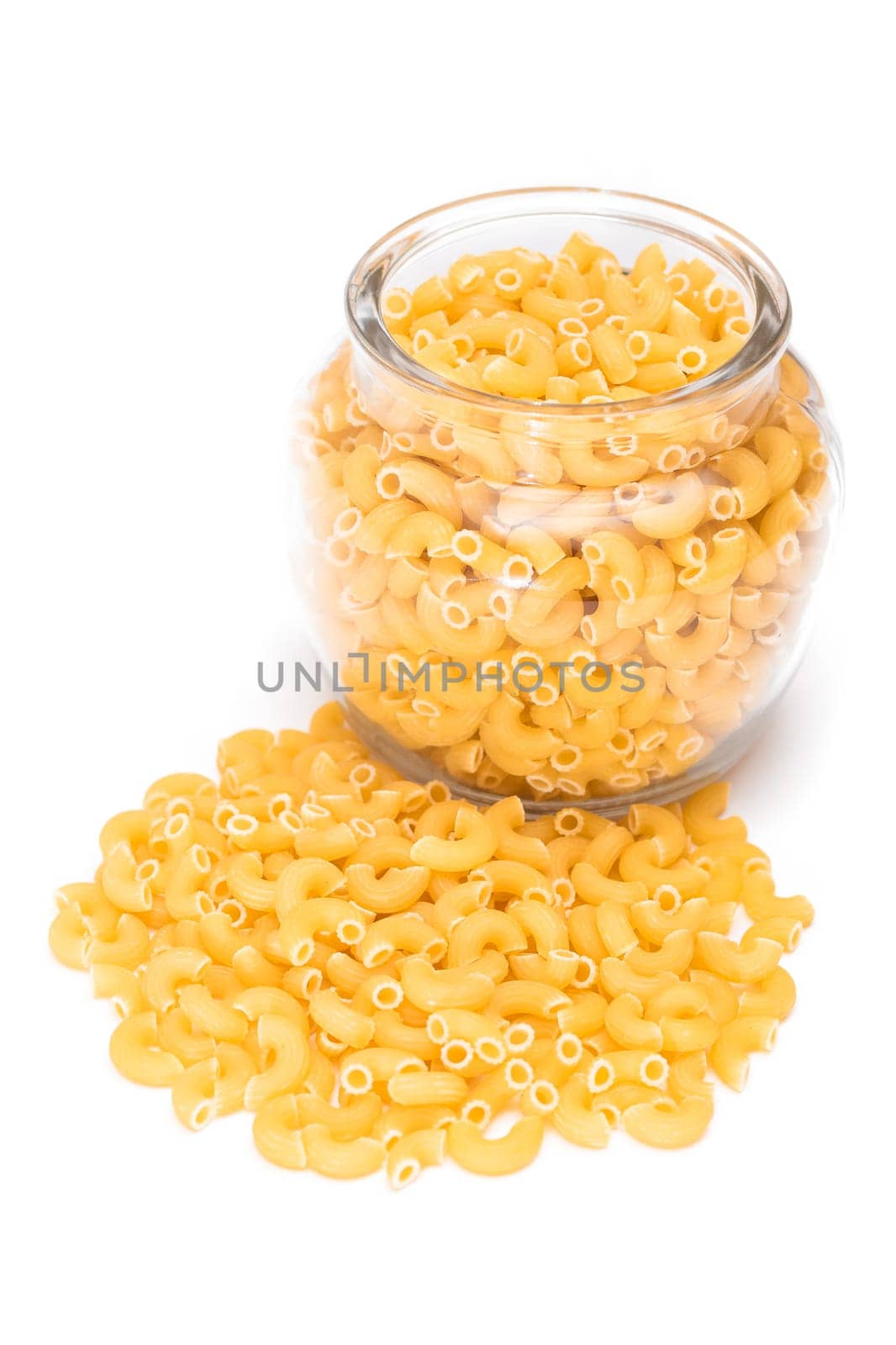 Uncooked Chifferi Rigati Pasta in Glass Jar Isolated on White Background. Fat and Unhealthy Food. Scattered Classic Dry Macaroni. Italian Culture and Cuisine. Raw Pasta