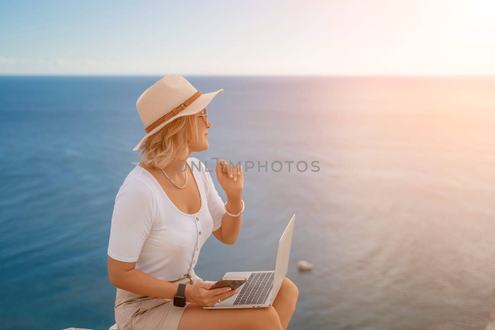 Freelance women sea working on the computer. Good looking middle aged woman typing on a laptop keyboard outdoors with a beautiful sea view. The concept of remote work. by Matiunina