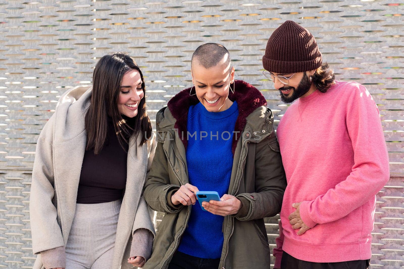 three smiling young friends enjoying the moment using together a mobile phone, concept of technology of communication and modern lifestyle