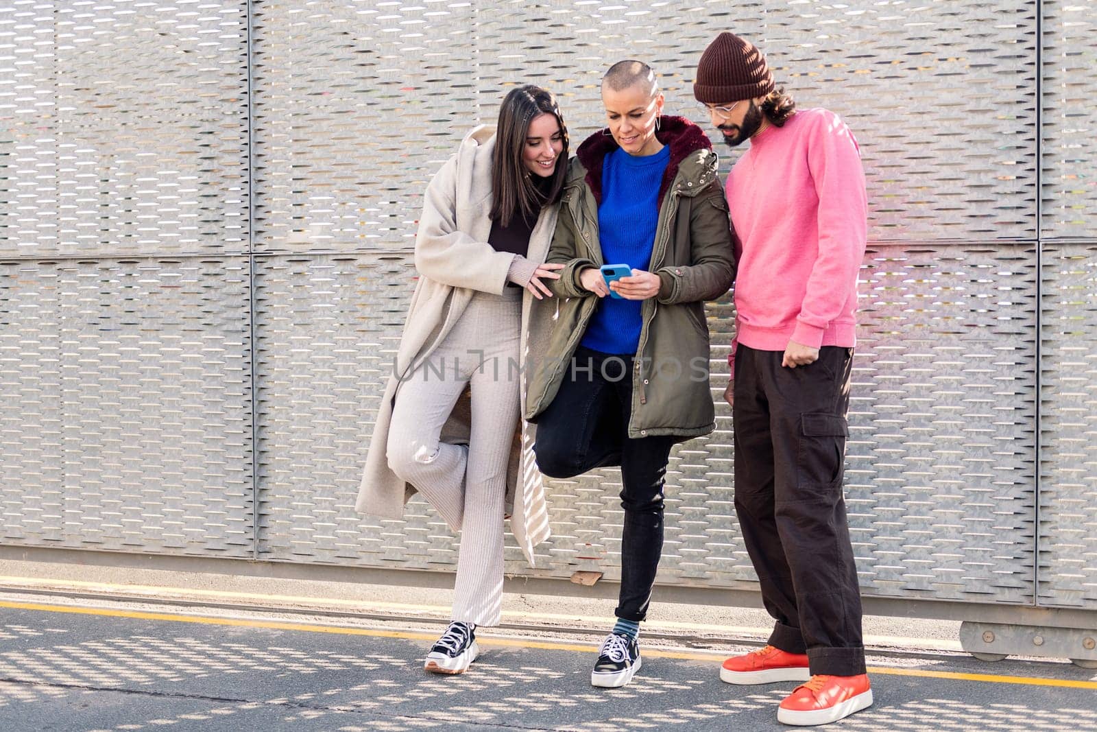 three happy young friends enjoying the moment using together a smart phone, concept of technology of communication and modern lifestyle, copy space for text