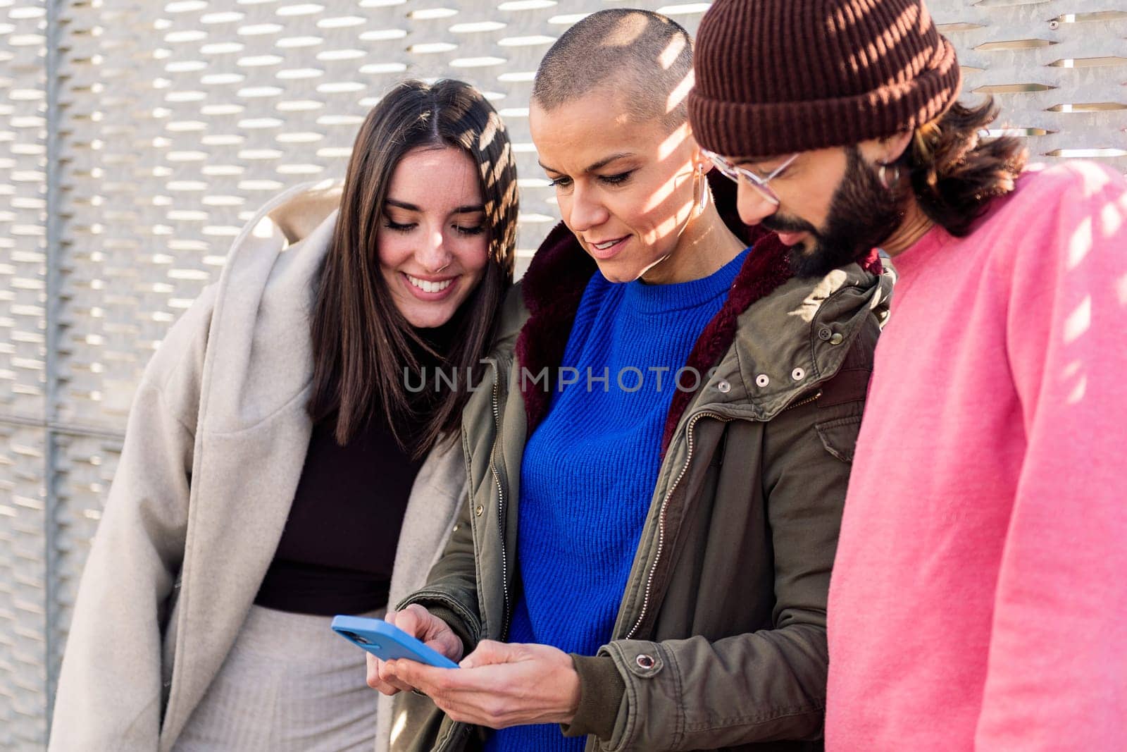 three young friends enjoying the moment using together a mobile phone, concept of technology of communication and modern lifestyle