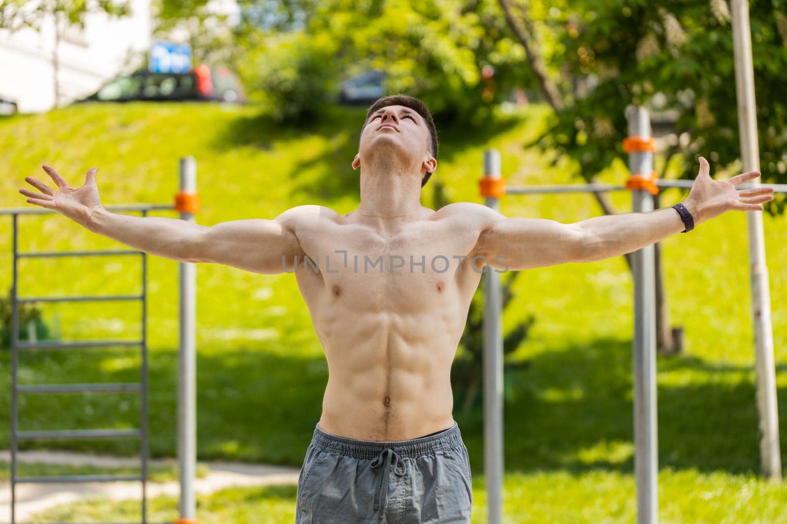 Athletic caucasian topless muscular man stretching body, warm up before cardio workout exercises. Young guy on playground. Sports, health, fitness routine workout. Strength and motivation. Outdoor gym